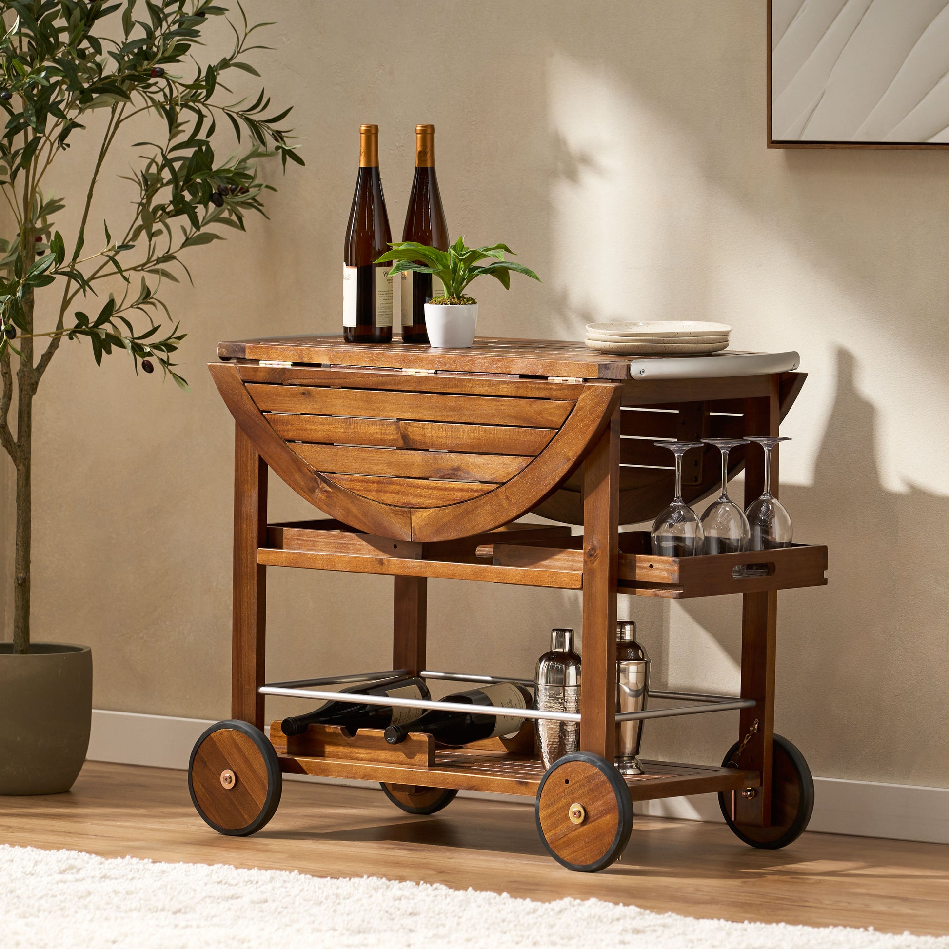 Wooden bar cart with dropleaf top holding wine bottles and a plant