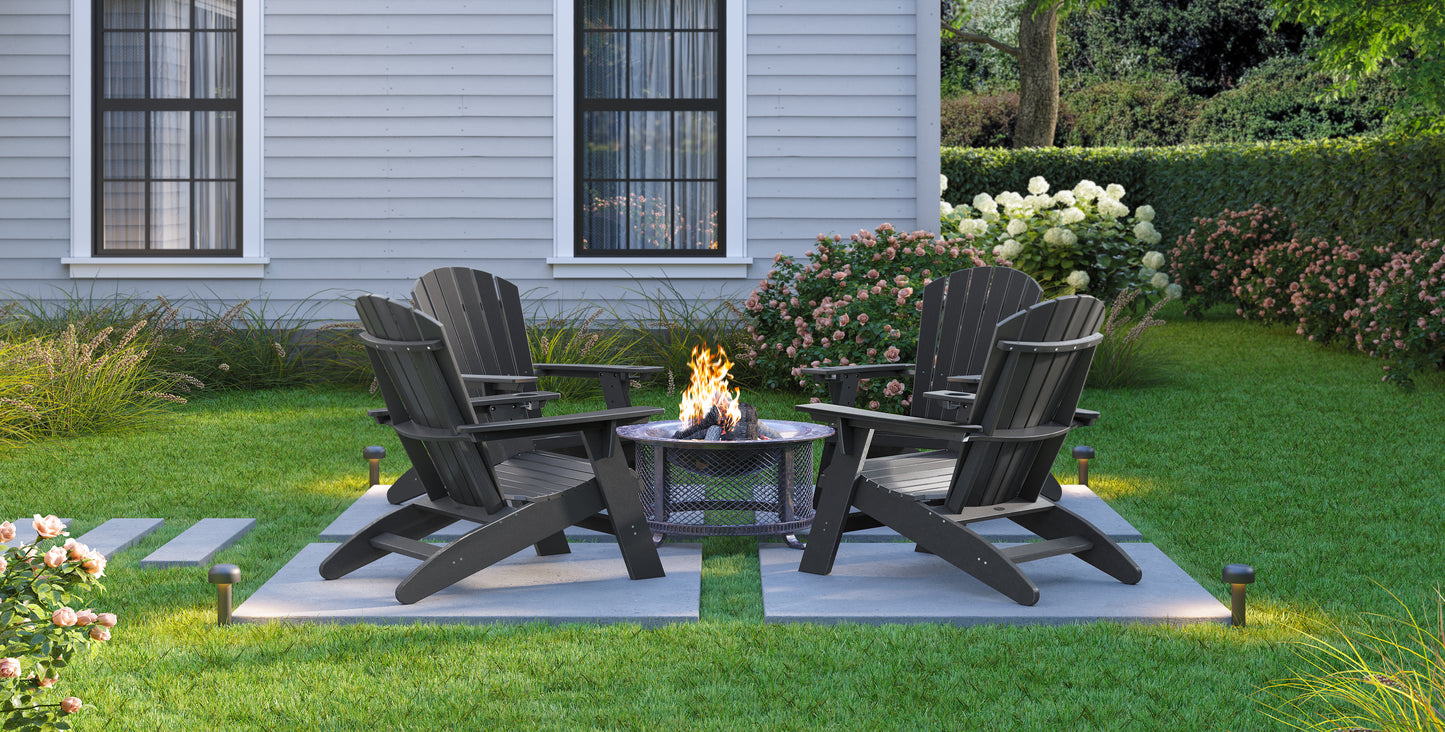 Four dark grey Adirondack chairs surround a lit fire pit on a stone patio in a lush green backyard setting