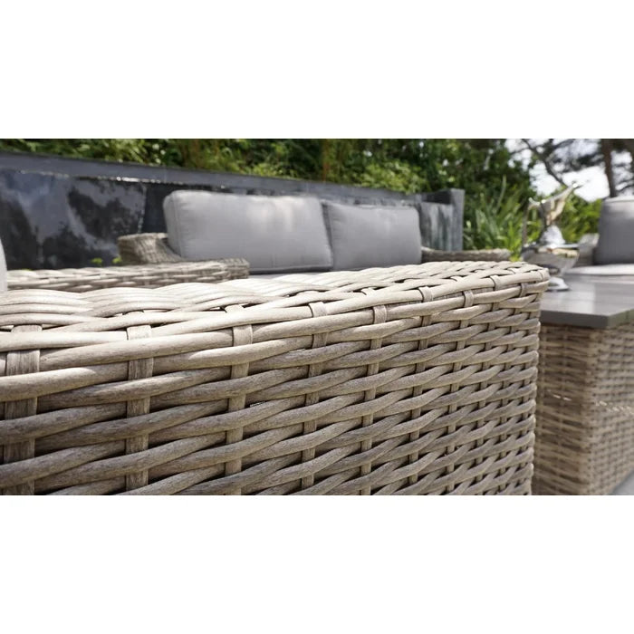 Closeup of a grey rattan outdoor sofa armrest with woven texture and light grey cushions