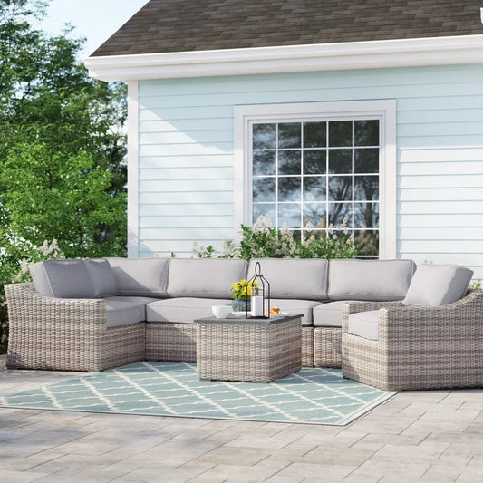 Grey wicker sectional sofa with plush cushions and a matching coffee table on a patio