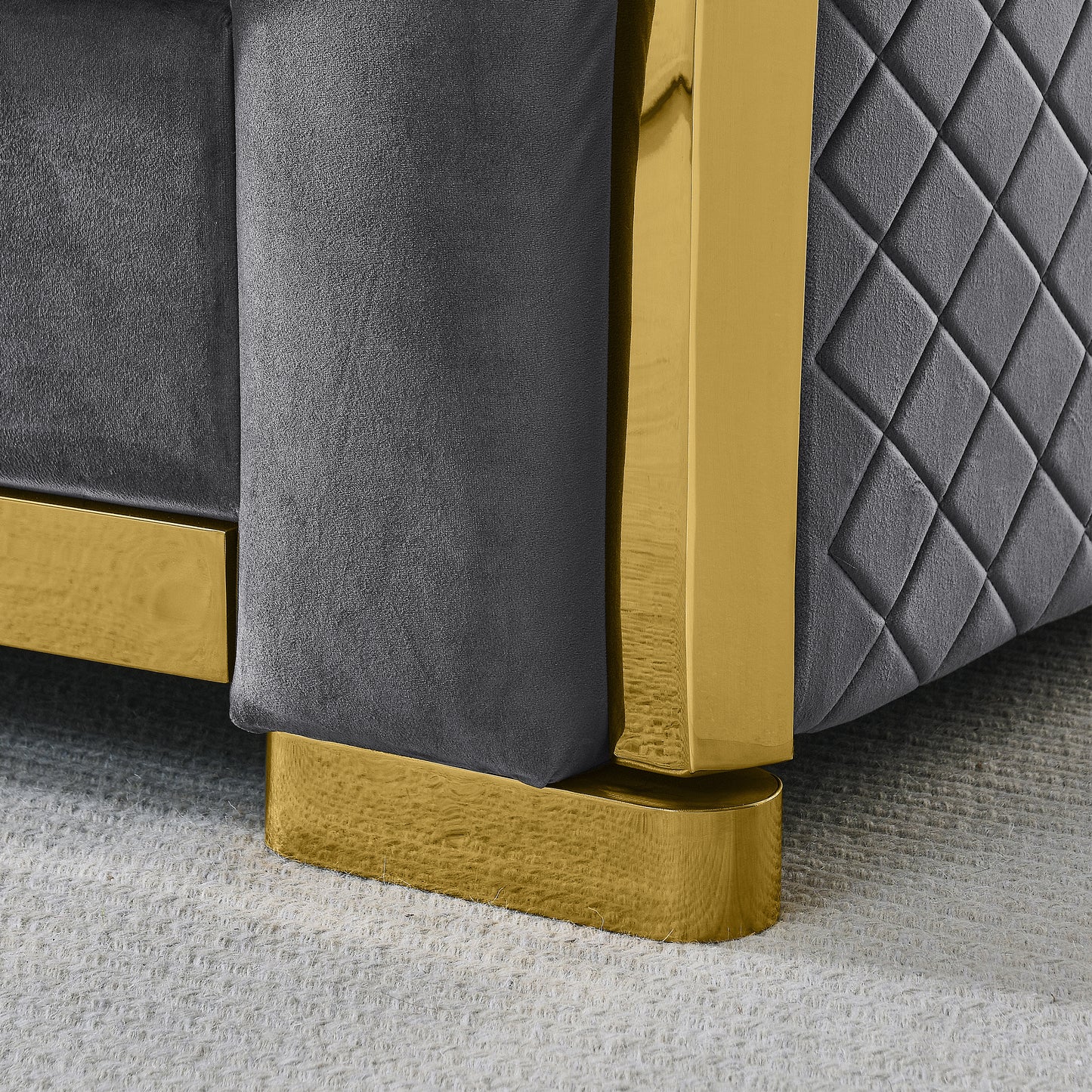 Closeup of a gray tufted velvet sofa with a polished gold metal leg accent