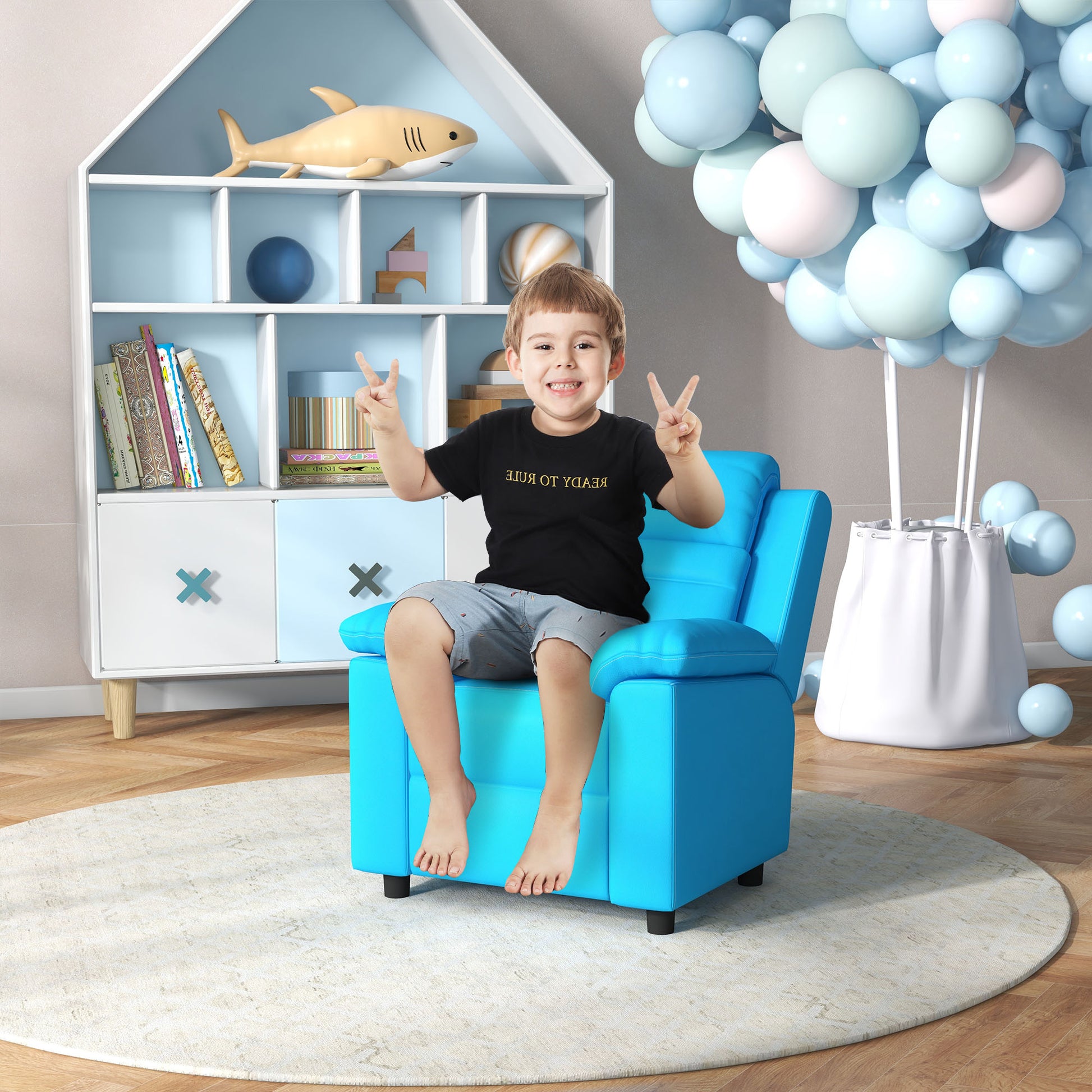 Toddler boy in black shirt and grey shorts sitting on bright blue accent chair