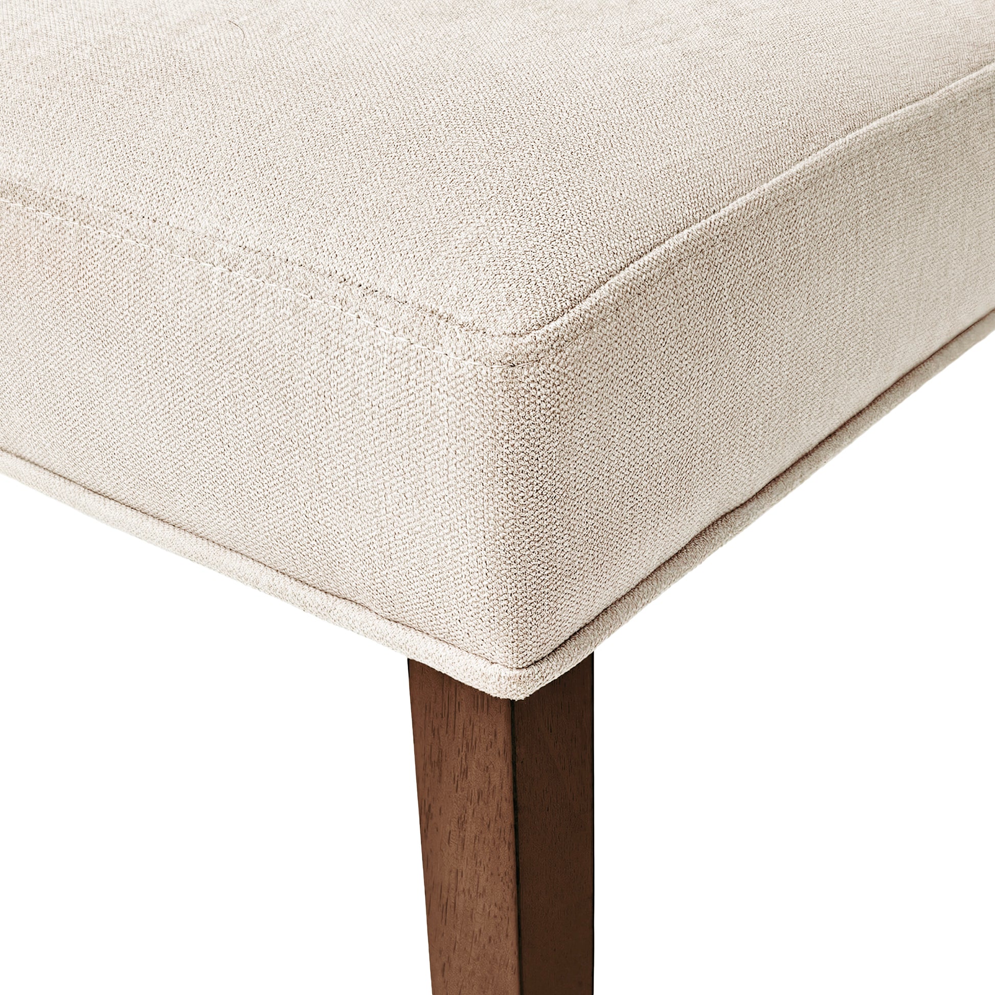 Closeup of a cream upholstered chair cushion with visible stitching and a dark wood leg