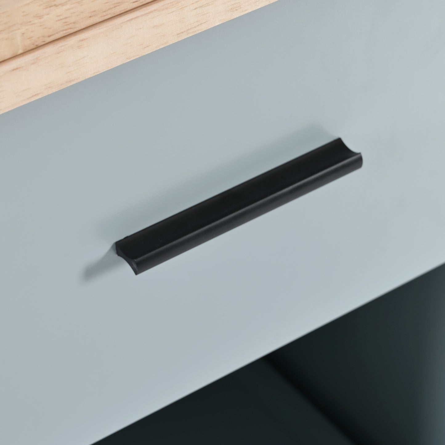 Black cabinet handle on a light blue drawer front with wood accent