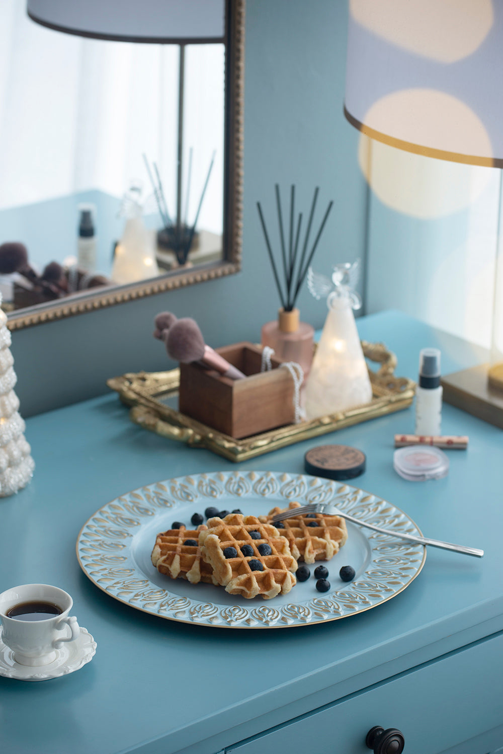 Three golden Belgian waffles with blueberries on a decorative blue plate served with coffee