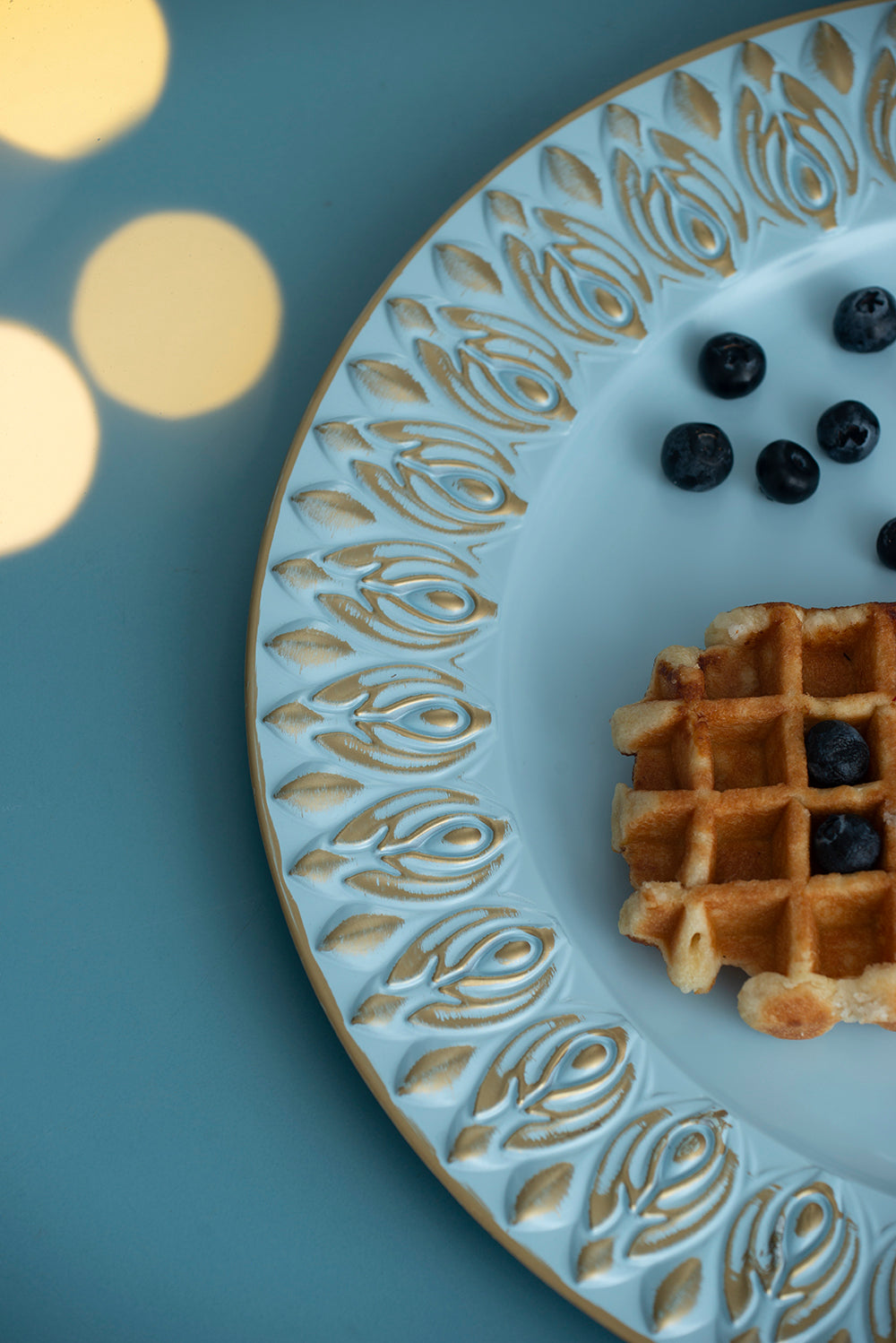 Light blue dinner plate with ornate gold trim and a single waffle with blueberries