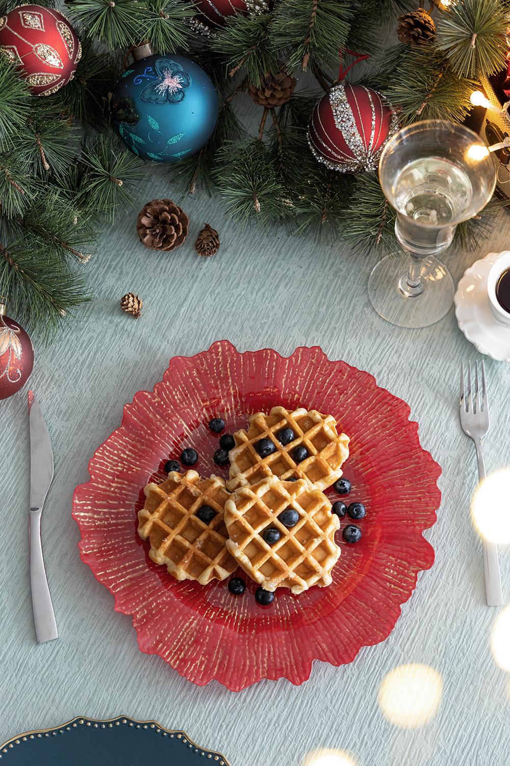 Three golden waffles topped with fresh blueberries on a red ruffled plate