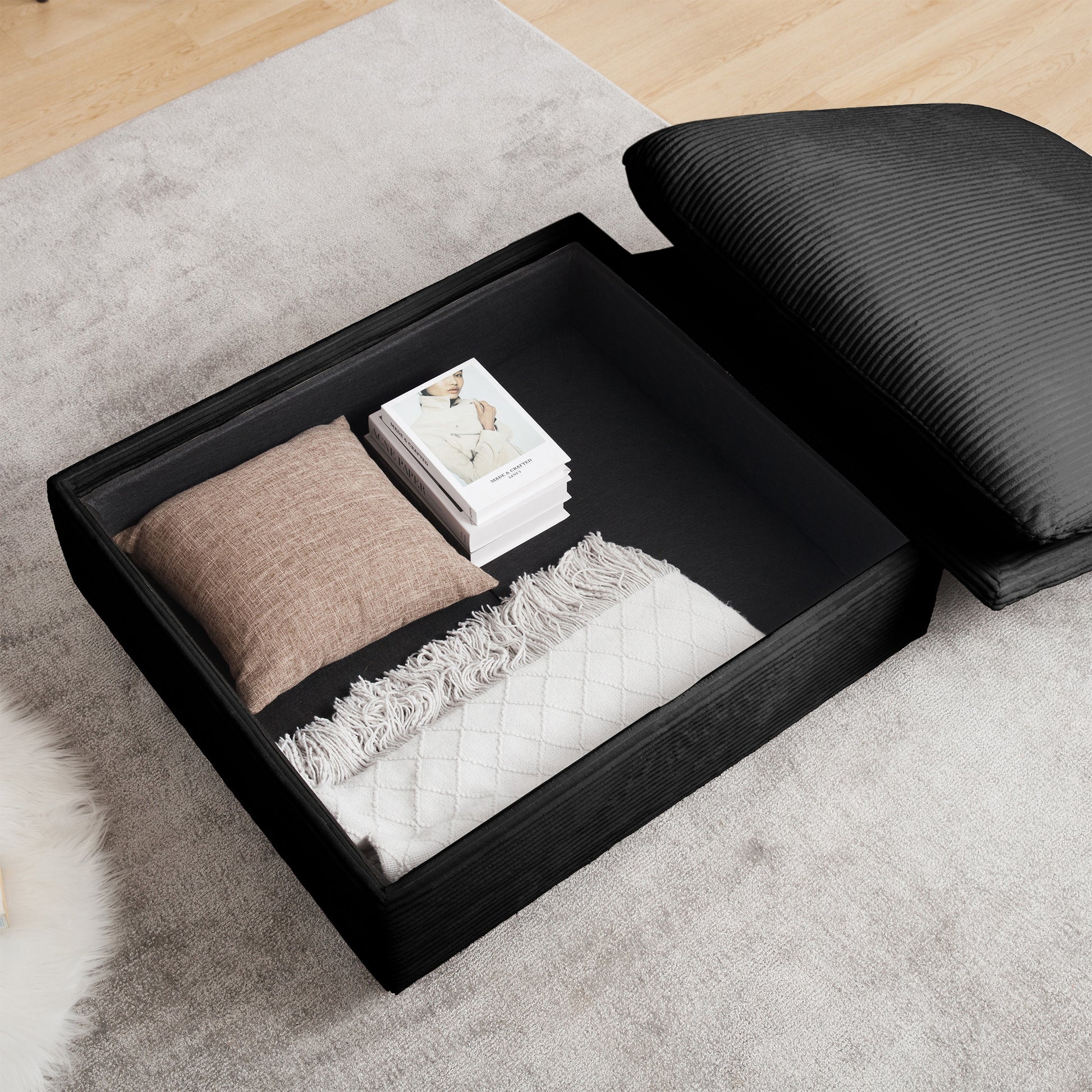 Black storage ottoman with open lid revealing linen pillow white throw and books