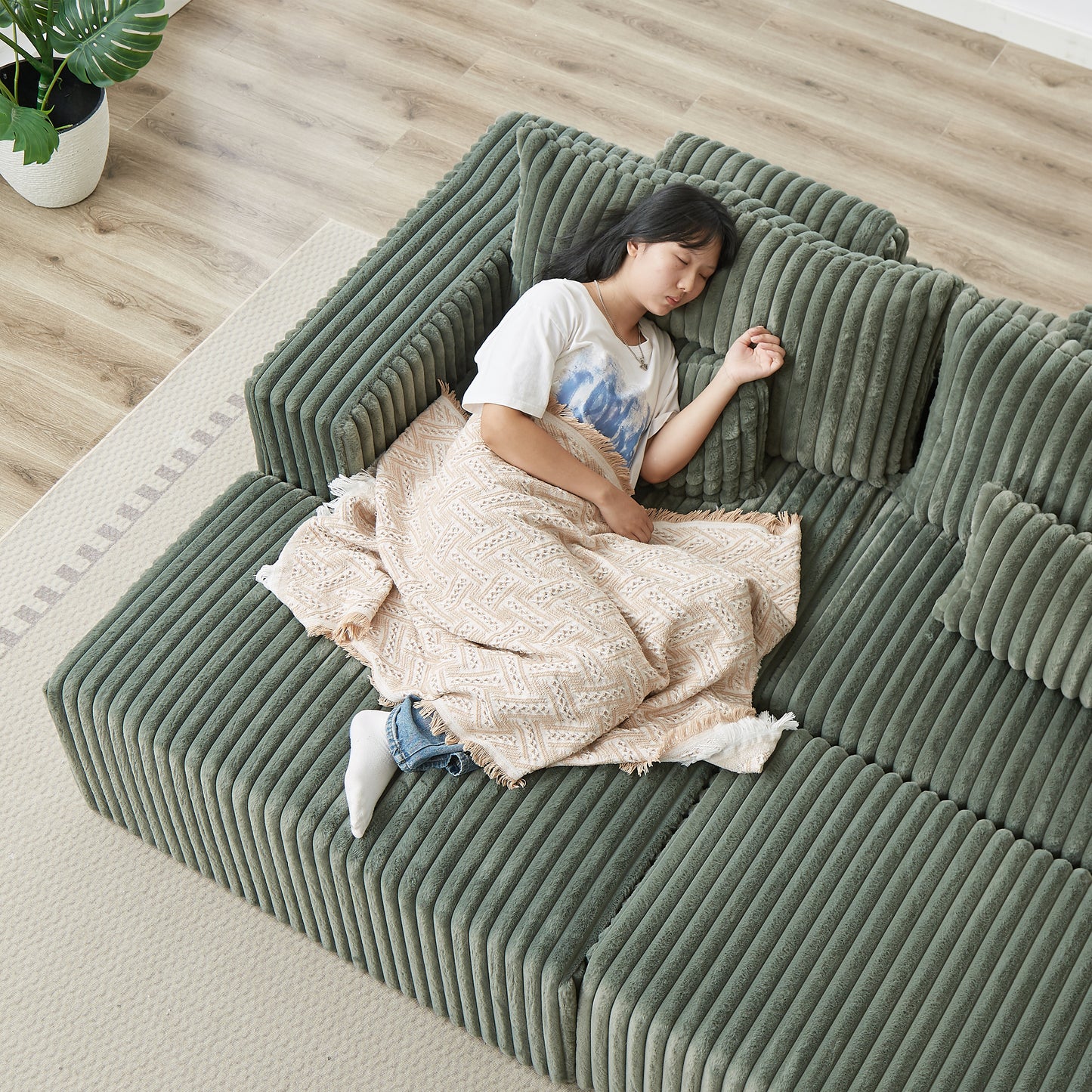 Green corduroy sectional sofa with a sleeping child and a patterned throw blanket