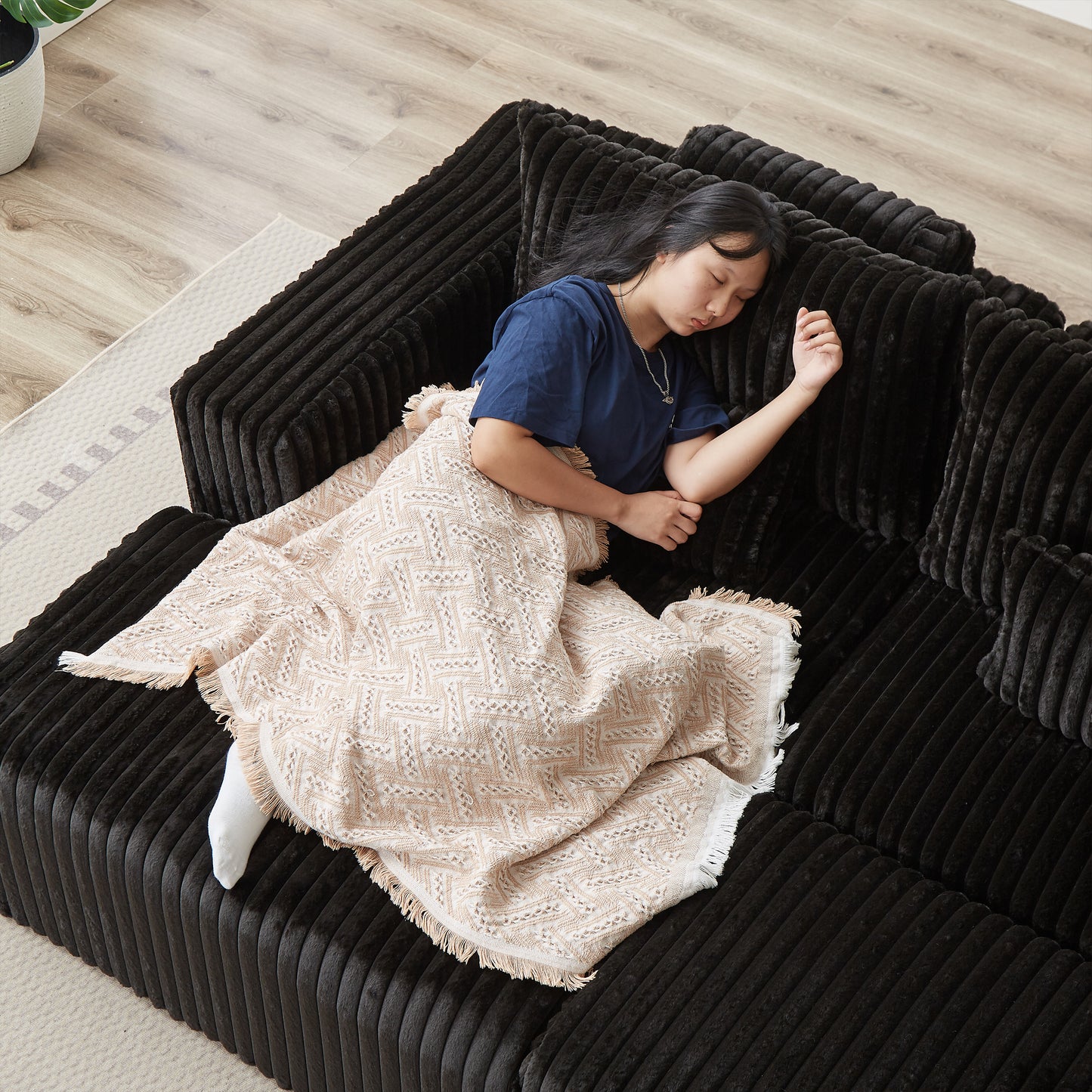 Girl sleeping on a plush black sofa covered with a cream textured throw blanket