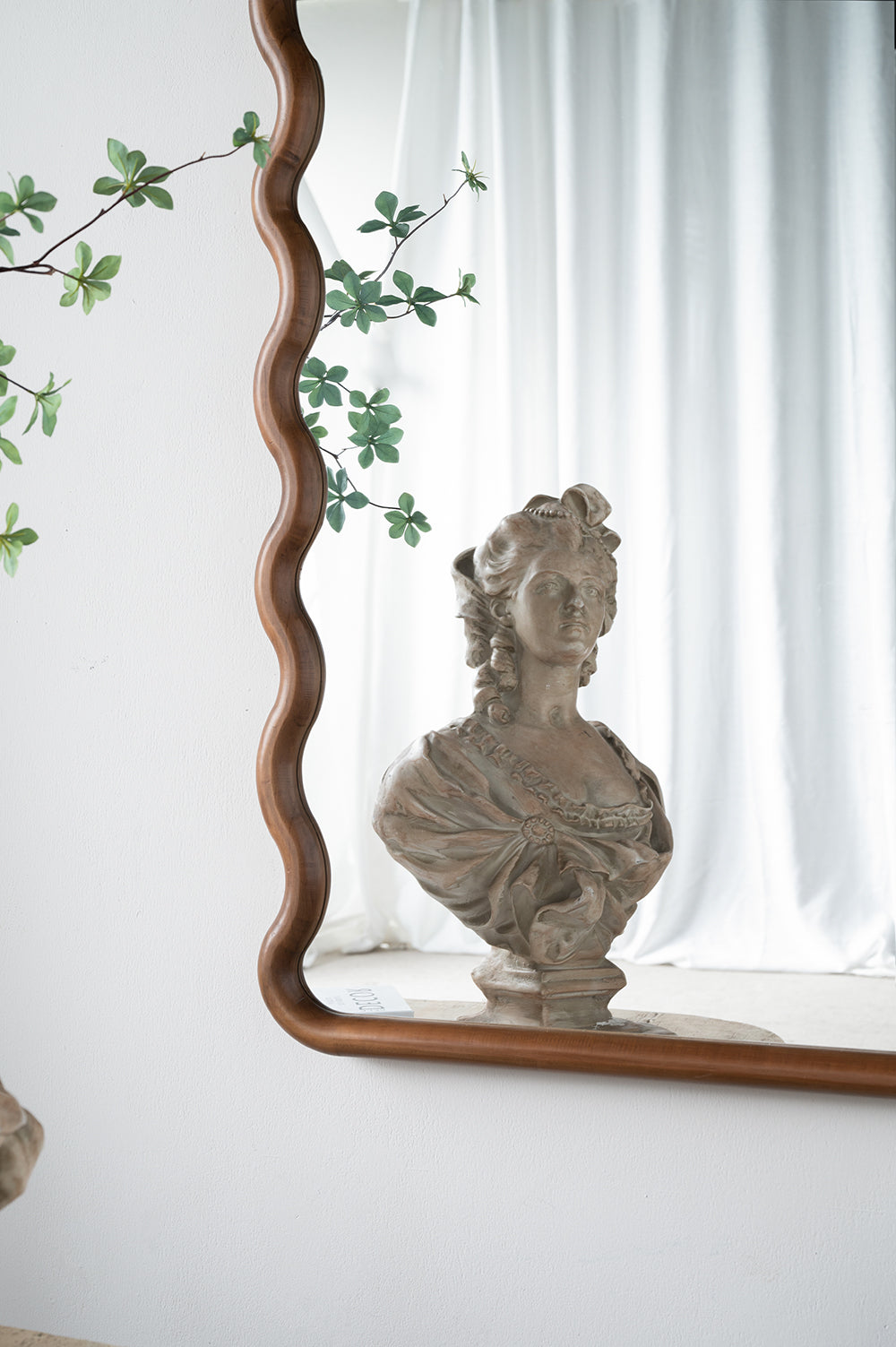 Vintage sculpted bust of a woman in ornate attire displayed in a wavy woodframed mirror