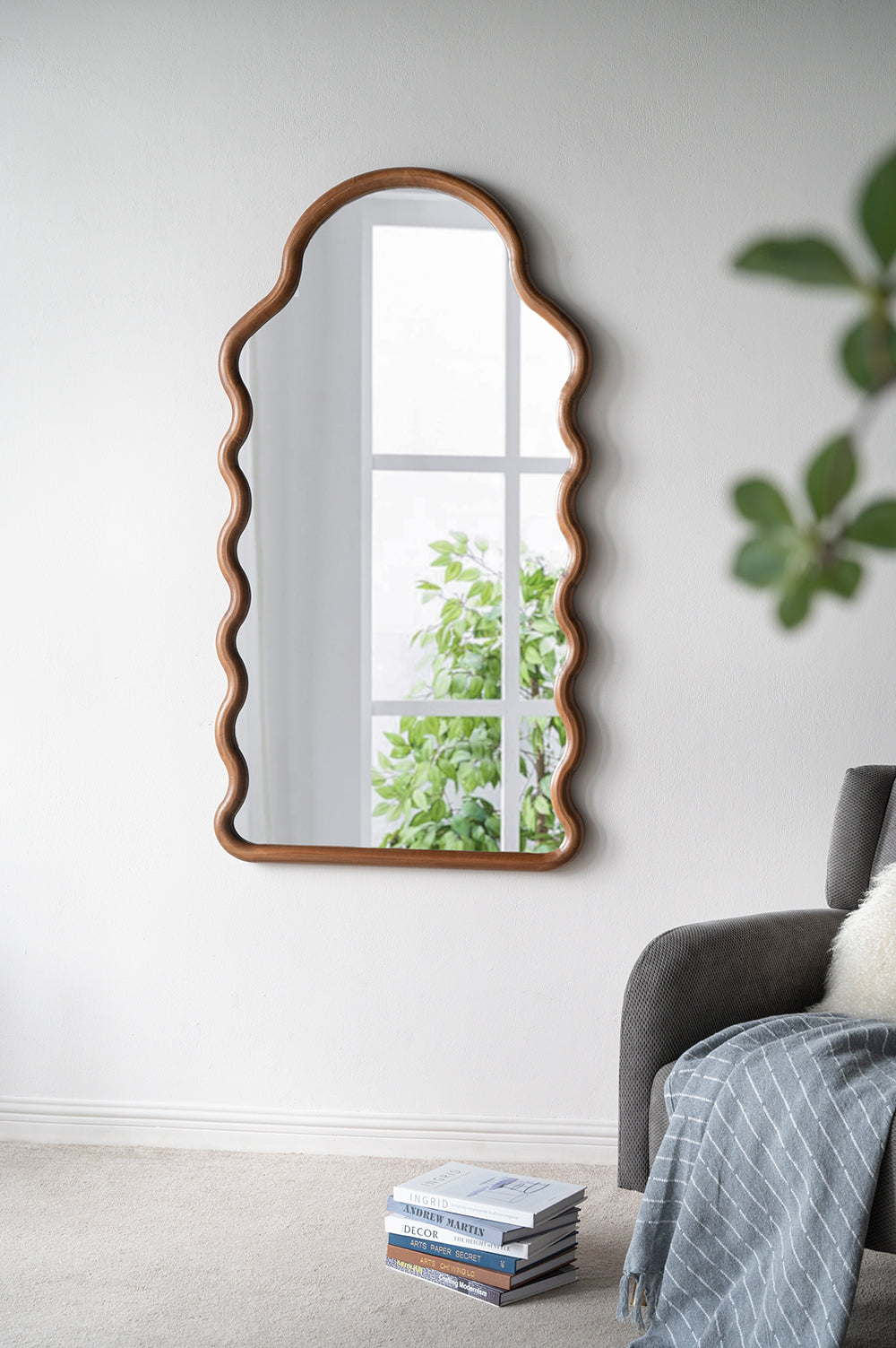 Irregular wooden framed mirror with wavy edges reflecting a bright window and green leaves