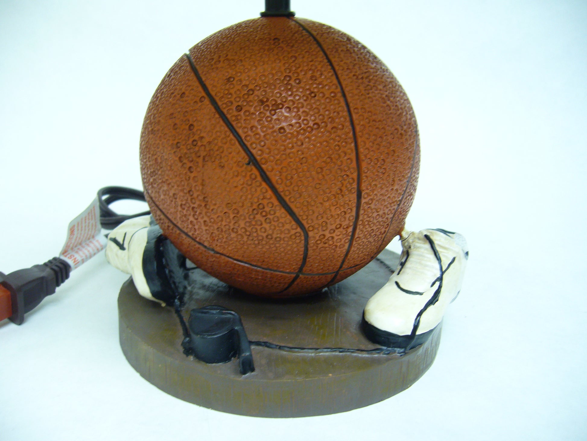 Basketballthemed lamp base with tiny white sneakers on a brown platform