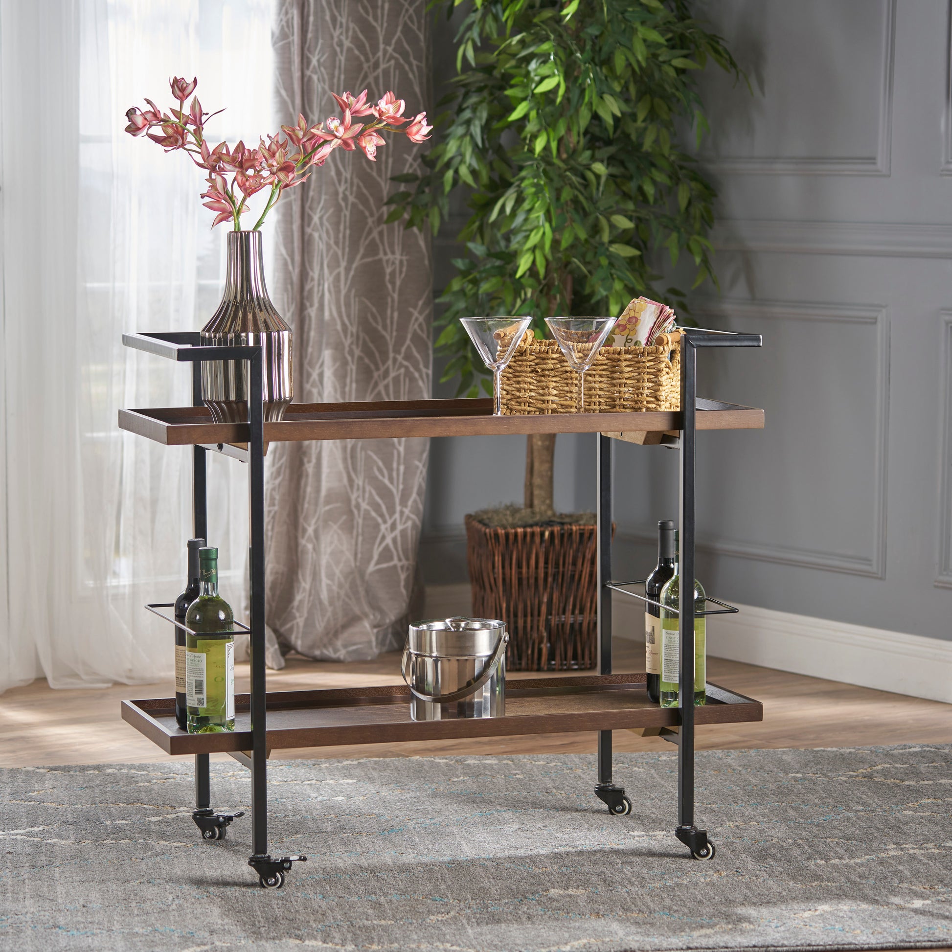 Twotier wooden bar cart with black metal frame holding wine bottles and glasses