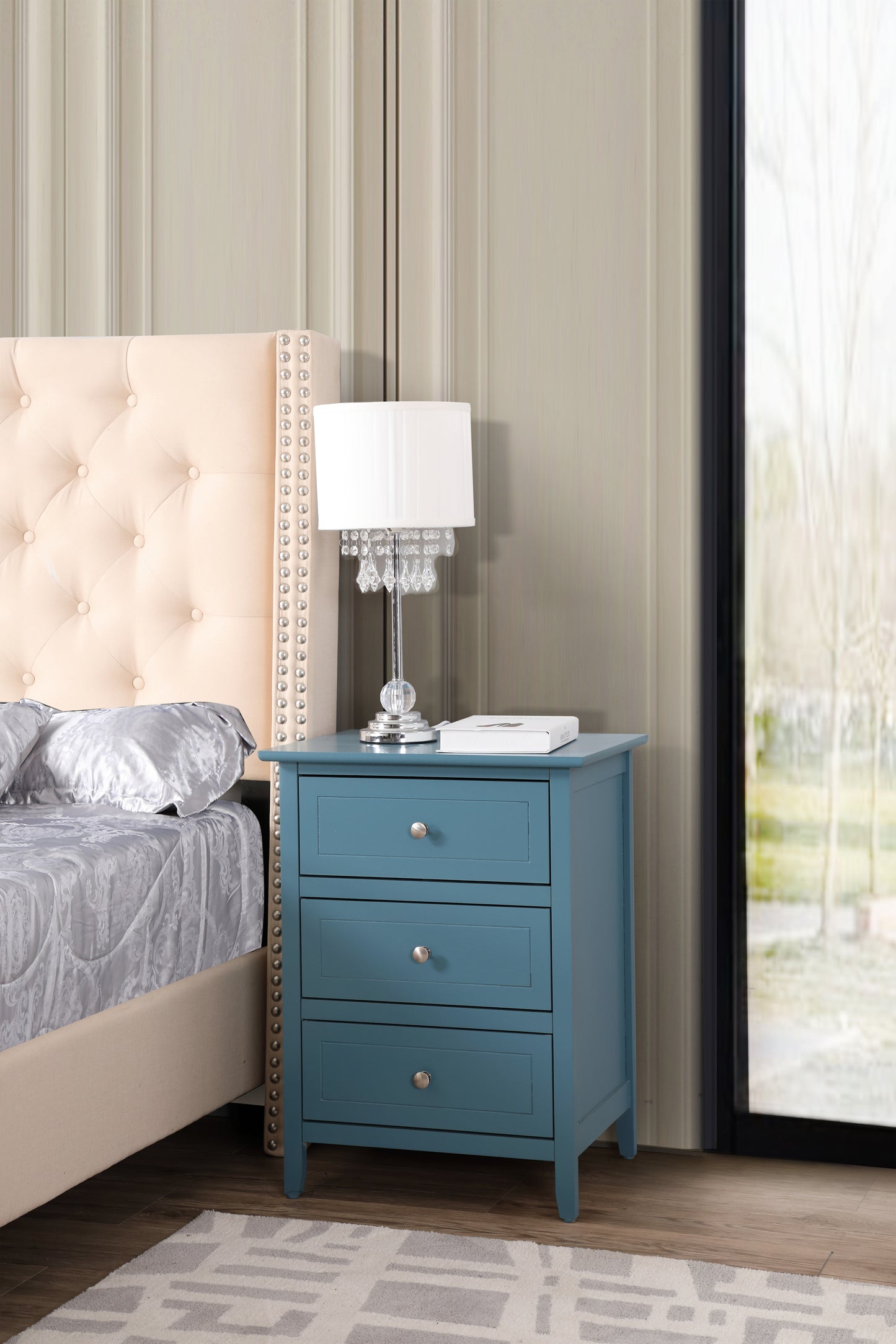Teal threedrawer wooden nightstand with silver knobs beside a bed