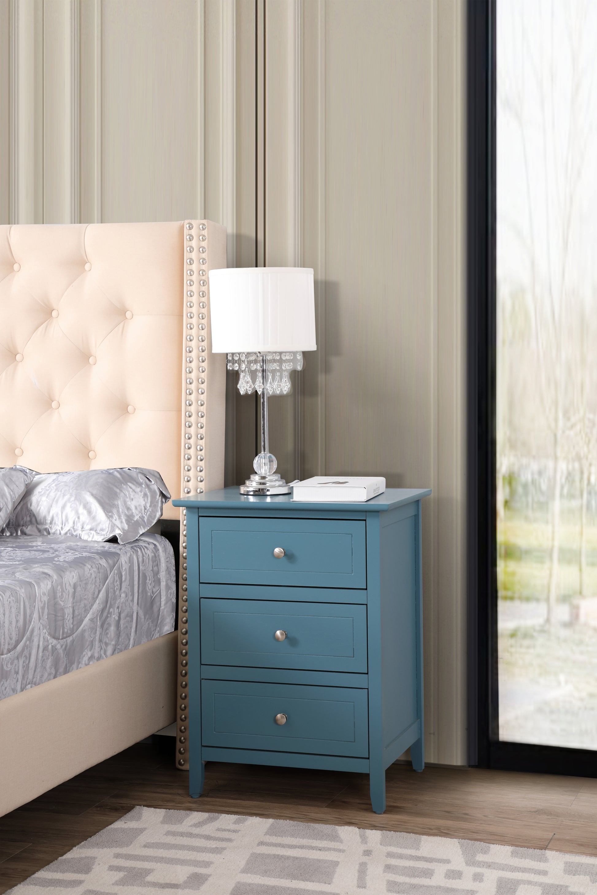 Teal threedrawer wooden nightstand with silver knobs beside a bed