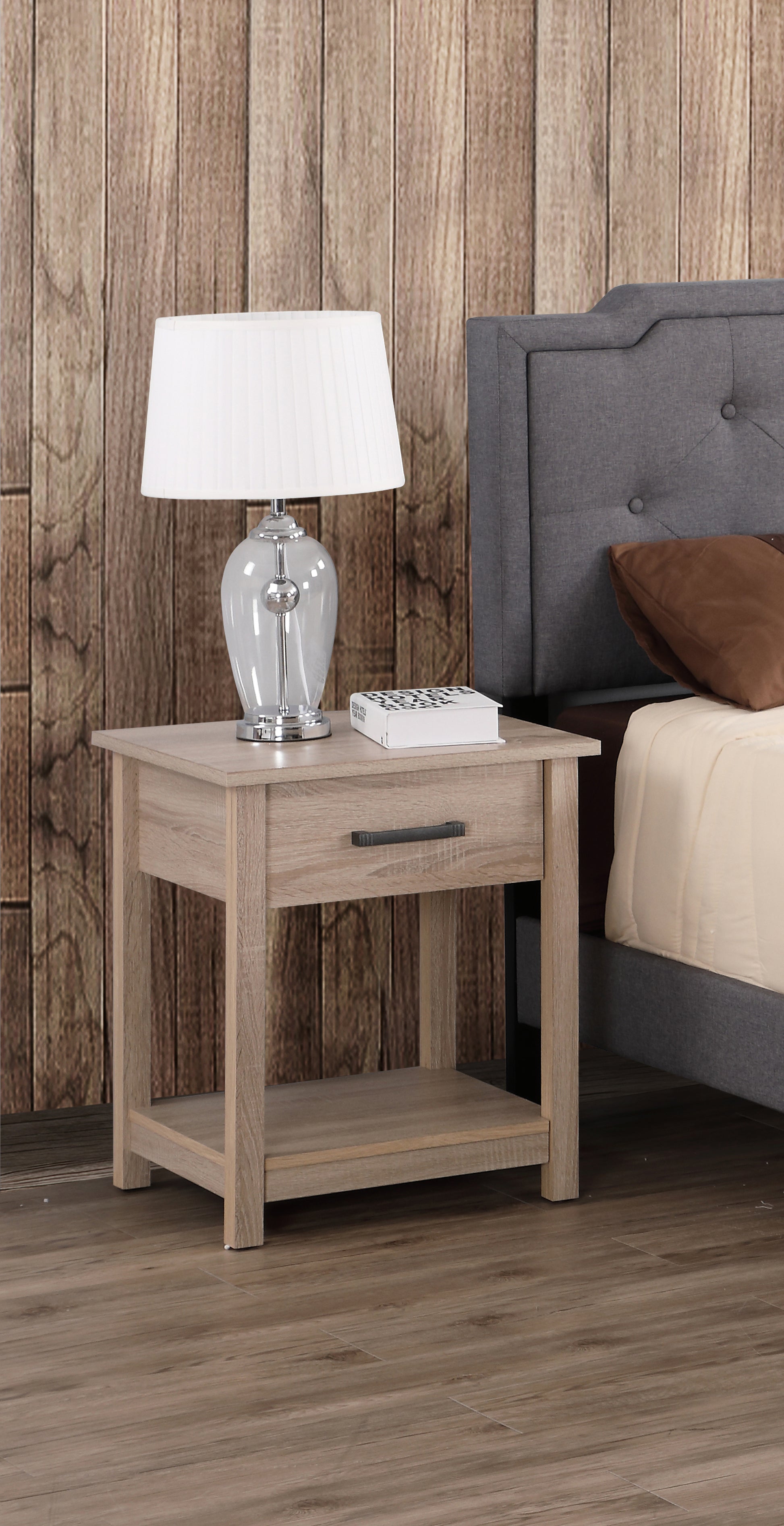 Light oak bedside table with drawer and shelf next to a grey upholstered bed