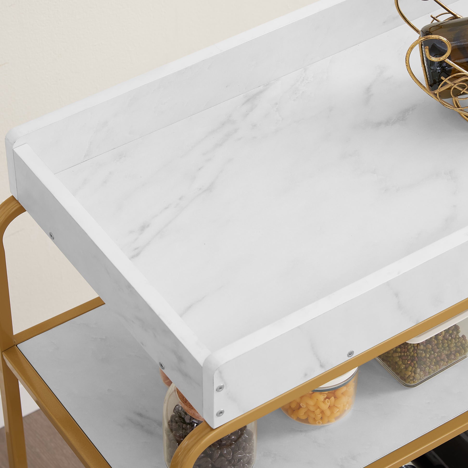 Gold metal bar cart with white marble finish shelves holding glass jars of beans and pasta