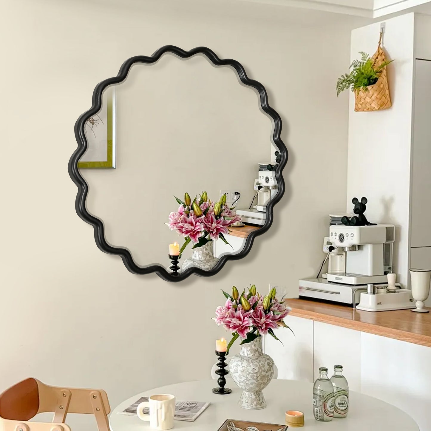 Round black wavy mirror reflecting pink lilies and a candle in a modern kitchen setting