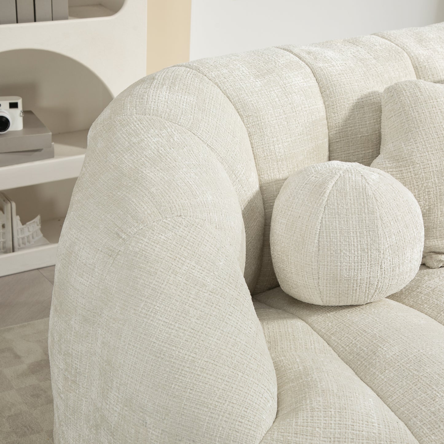 Closeup of a textured cream boucle sofa arm with piped seams and accent pillow