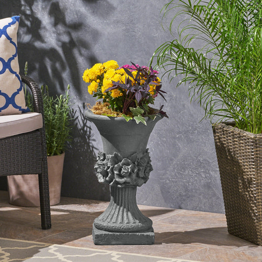 Ornate gray concrete garden urn with rose detailing and vibrant floral arrangement