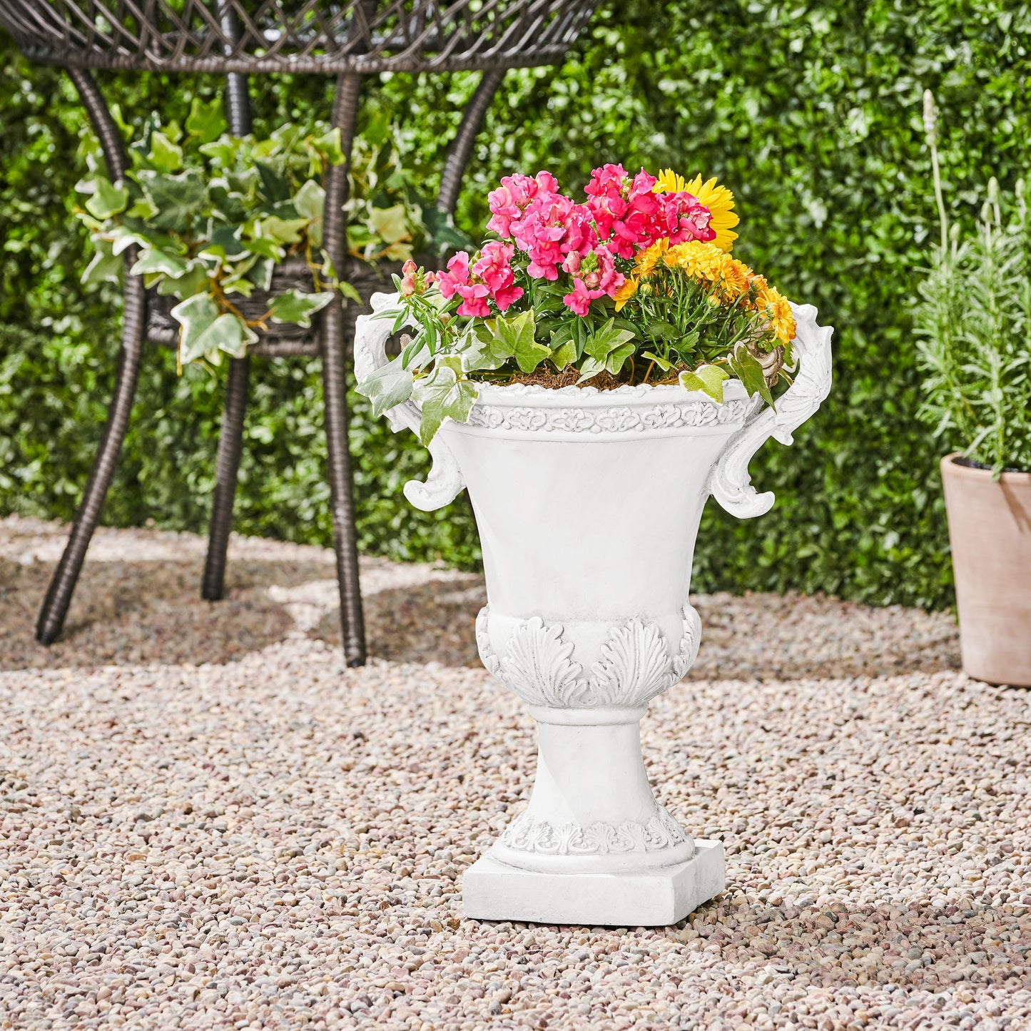 White ornate garden urn with pink and yellow flowers on gravel patio