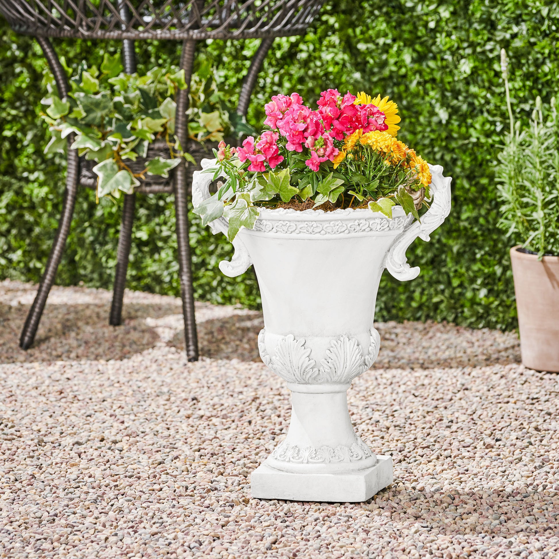 White ornate garden urn with pink and yellow flowers on gravel patio