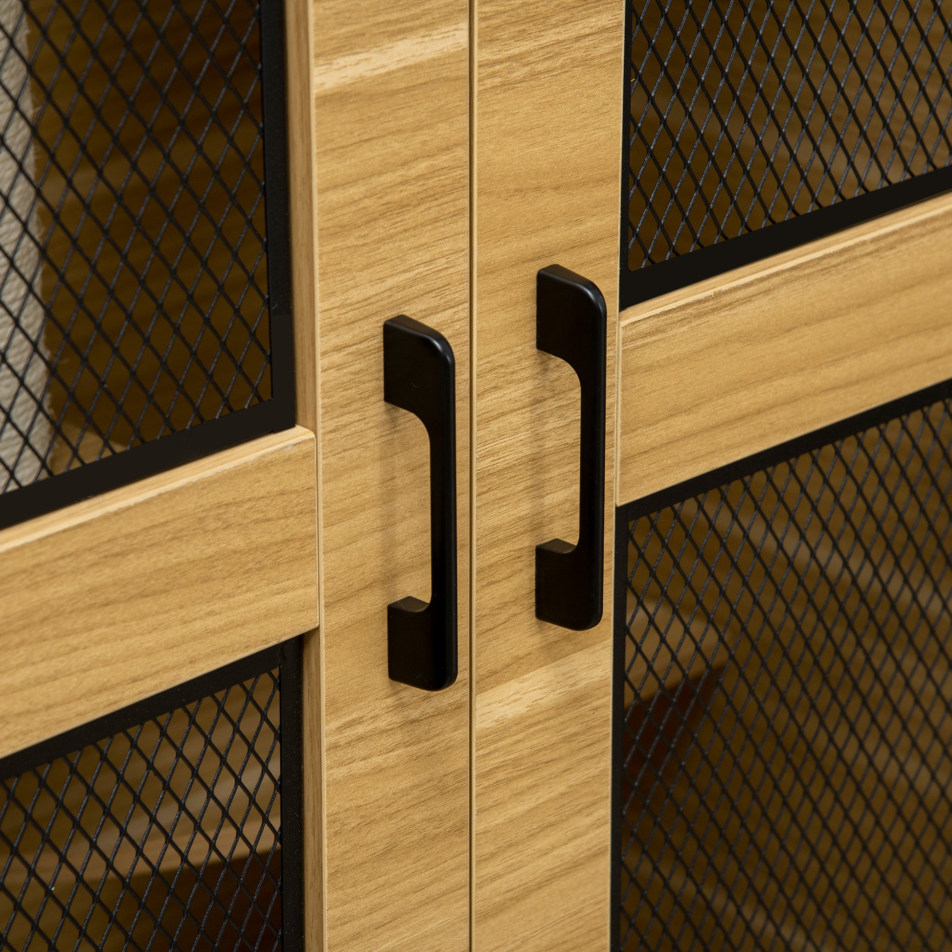 Closeup of two black handles on light wood cabinet doors with black wire mesh panels