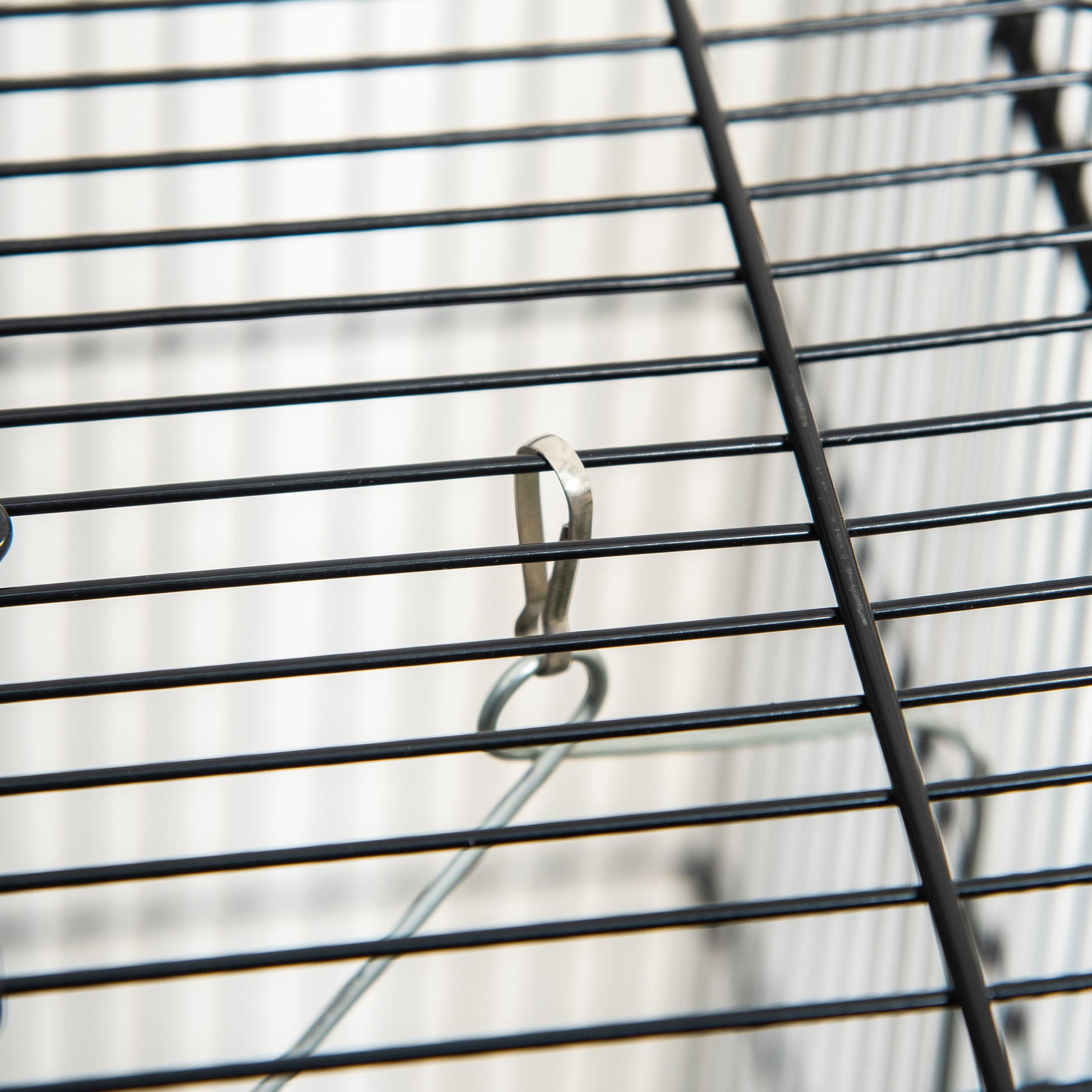 Closeup of a black metal cage grate with a silver clip attached to a wire hanger