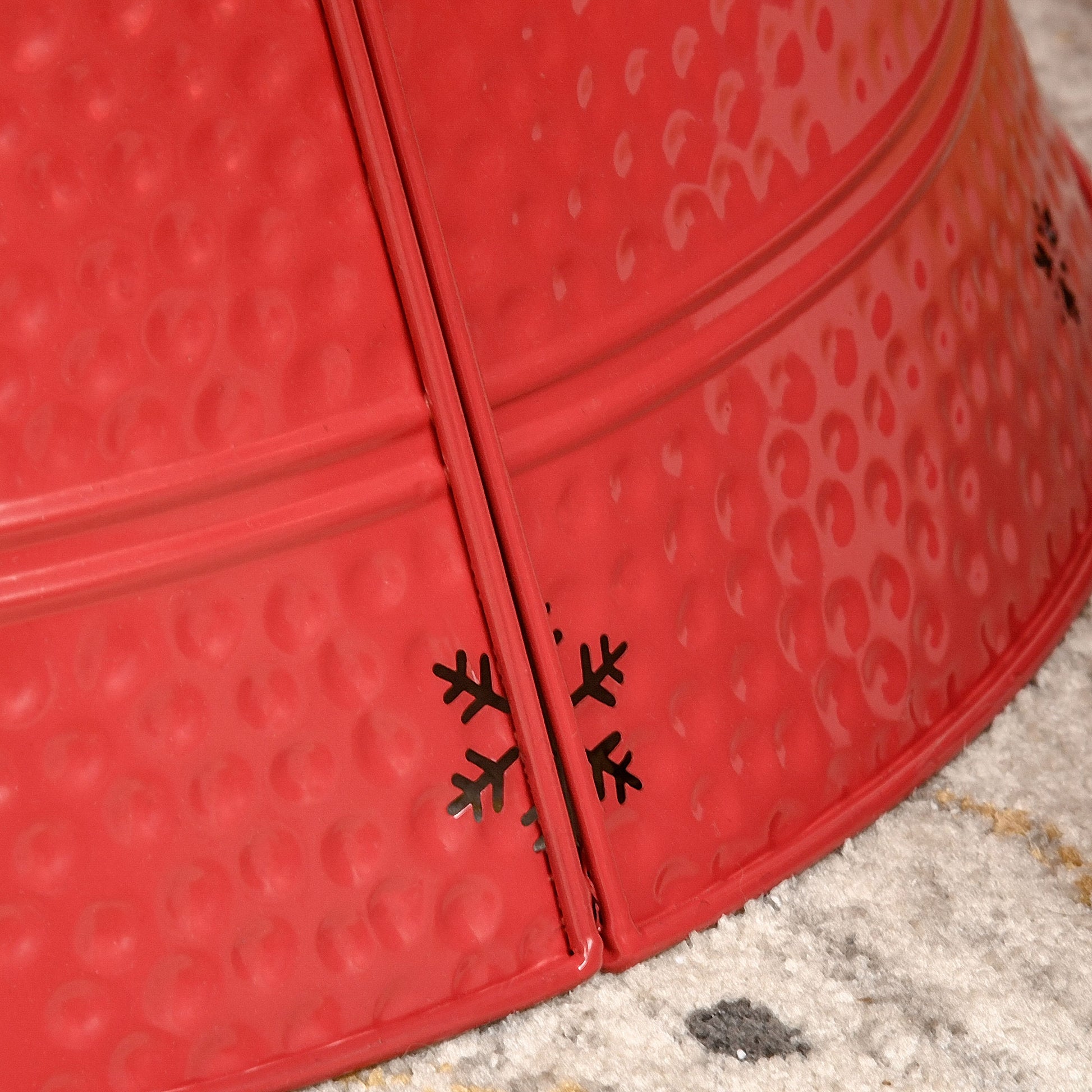 Closeup of red metal Christmas tree skirt with embossed snowflake cutouts