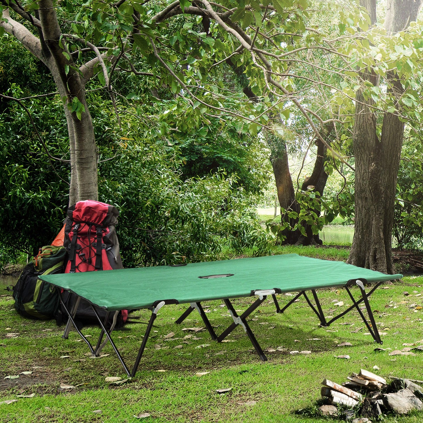Green camping cot with metal frame set up on grass near trees and backpacks