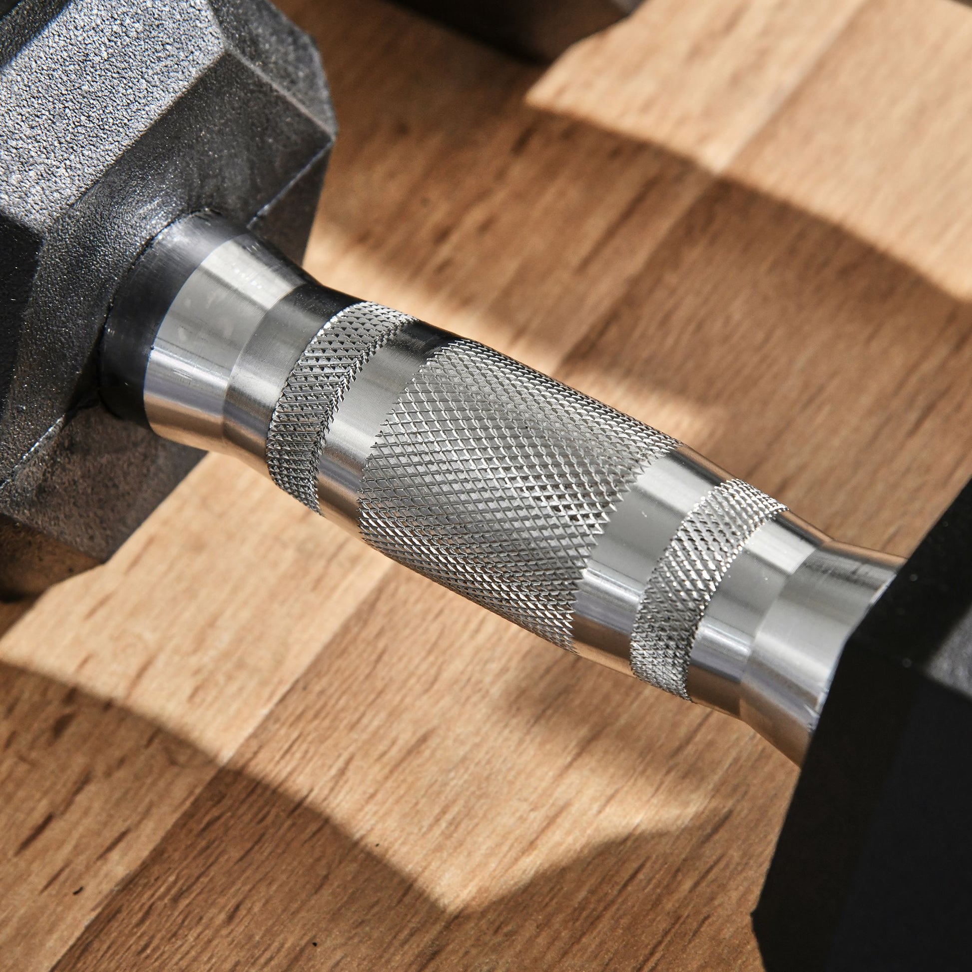 Closeup of hexagonal dumbbell with textured chrome handle on wooden floor