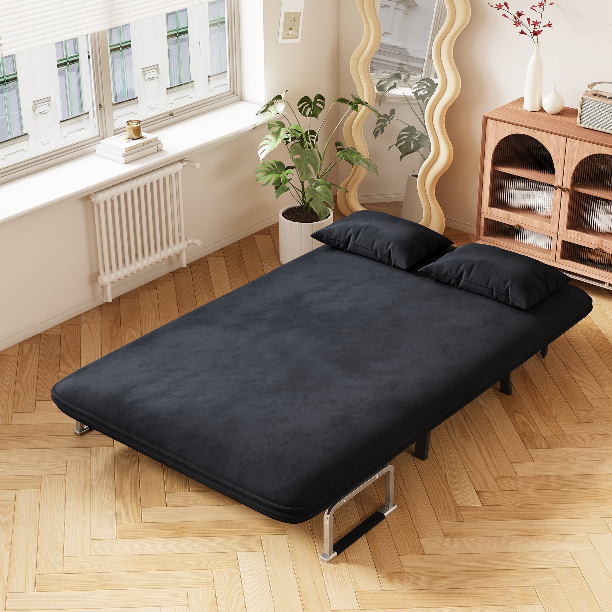 Dark grey velvet sofa bed with two black pillows on wooden floor