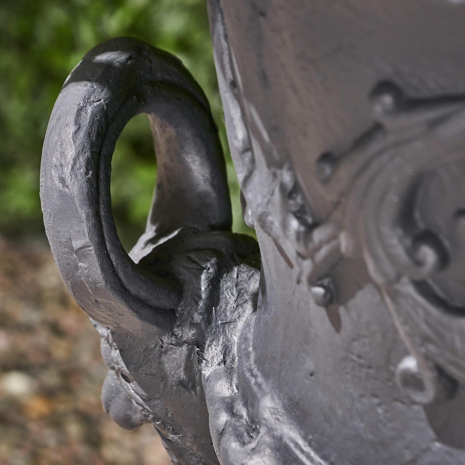 Closeup of a dark grey cast iron garden urn handle with intricate scrollwork details