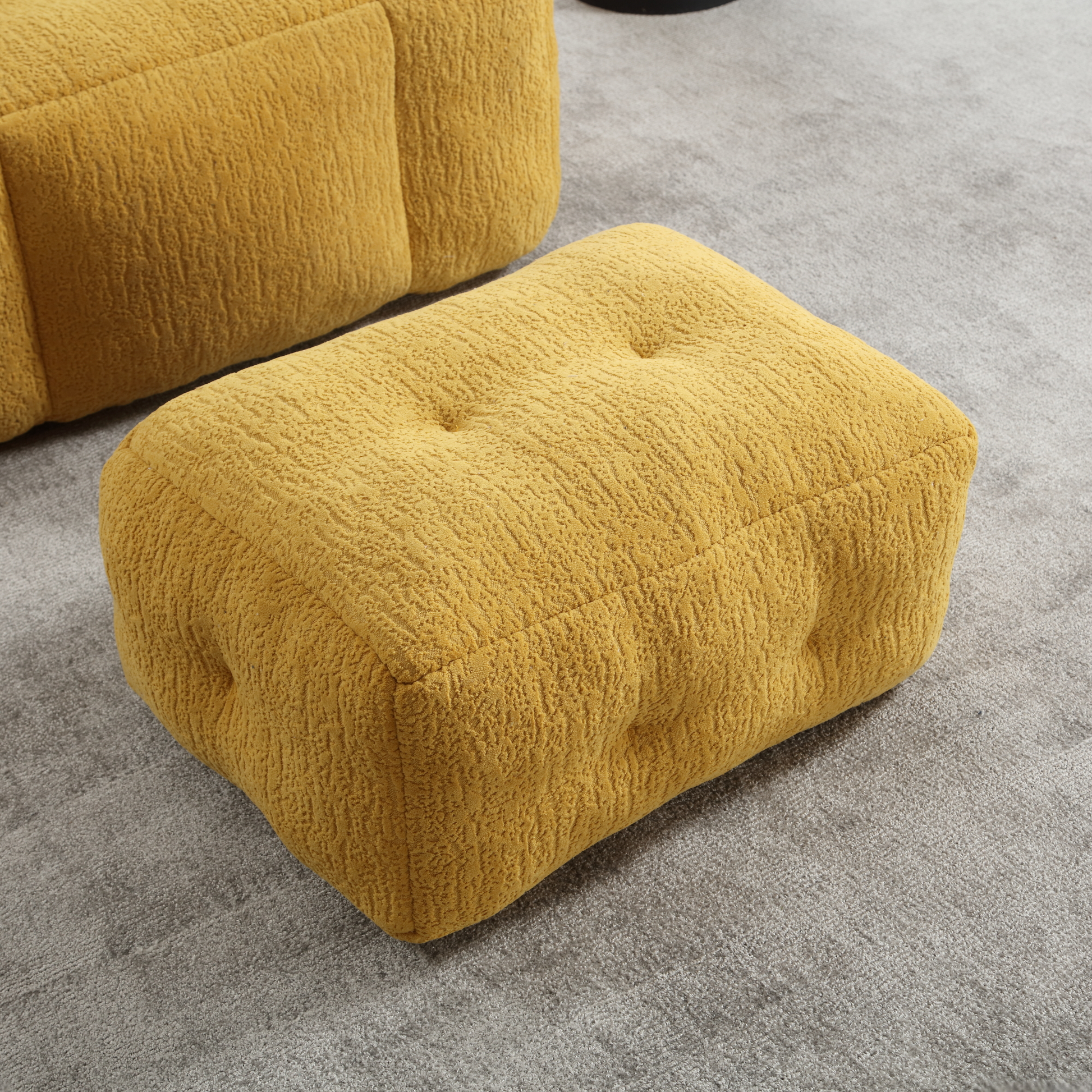 Textured mustard yellow ottoman with button tufting on a gray carpet floor