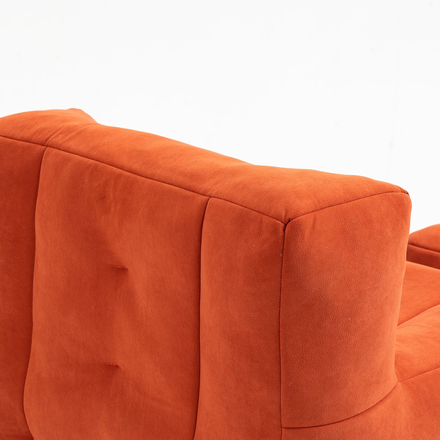 Closeup of plush orange velvet sofa back with tufted detailing and clean stitching