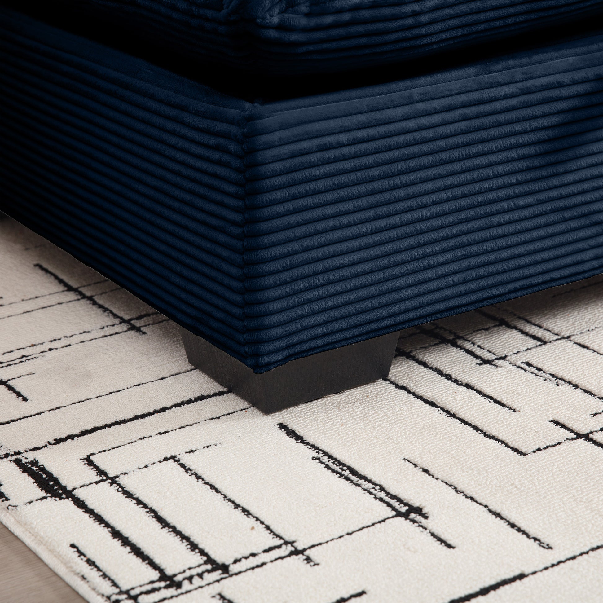 Navy blue corduroy sofa corner resting on a cream rug with abstract black lines