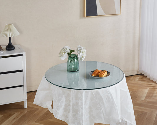 Round clear glass tabletop on a white floral tablecloth holding vase and pastries