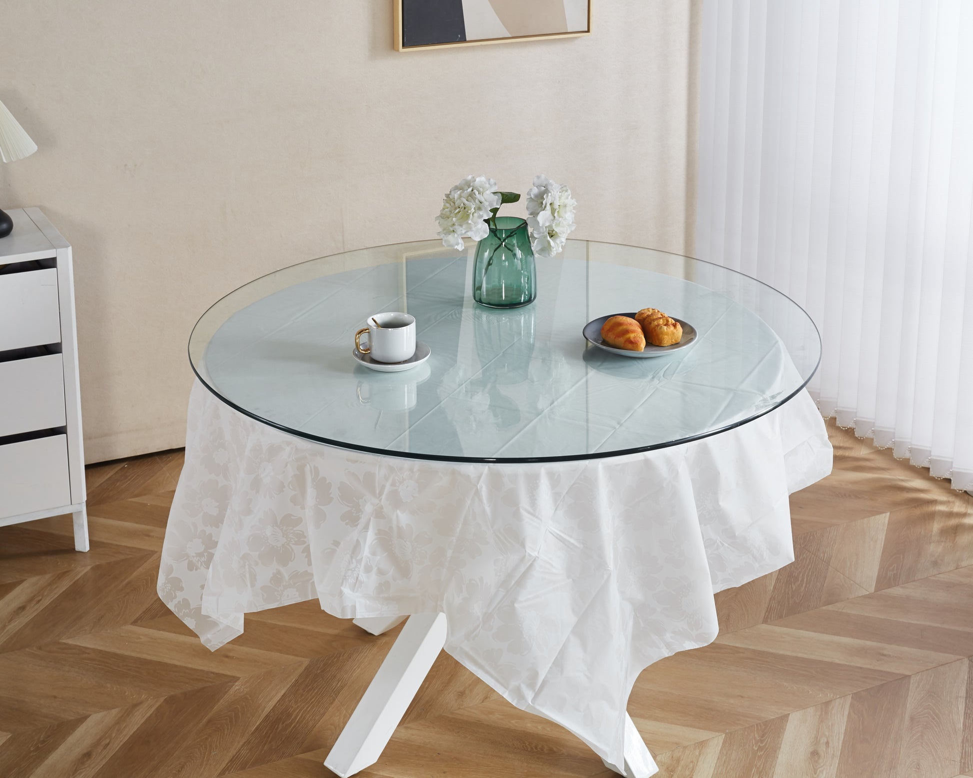 Elegant round glass dining table with a white floral tablecloth and a white mug with gold handle