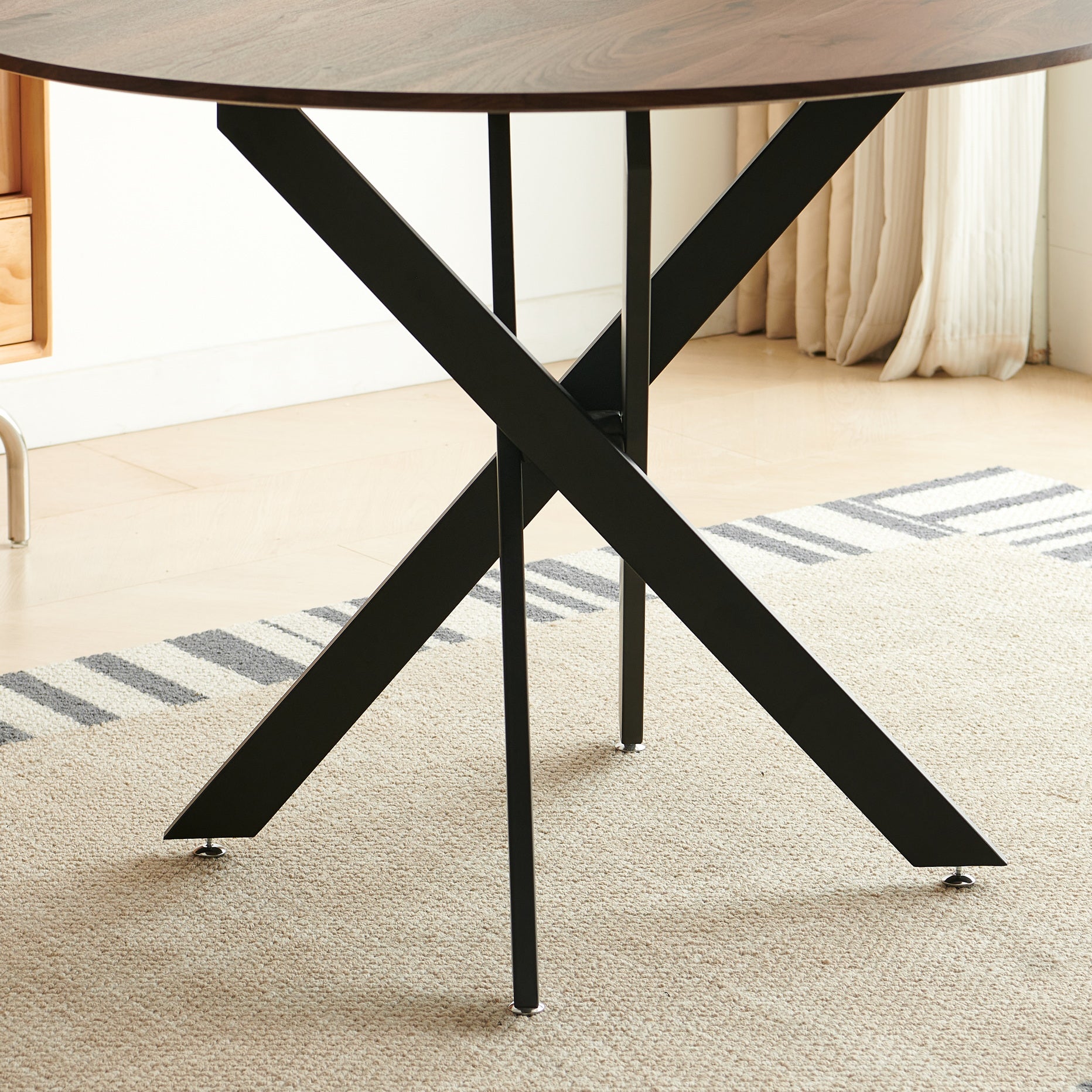 Dark wood round dining table with matte black metal pedestal base on a textured rug