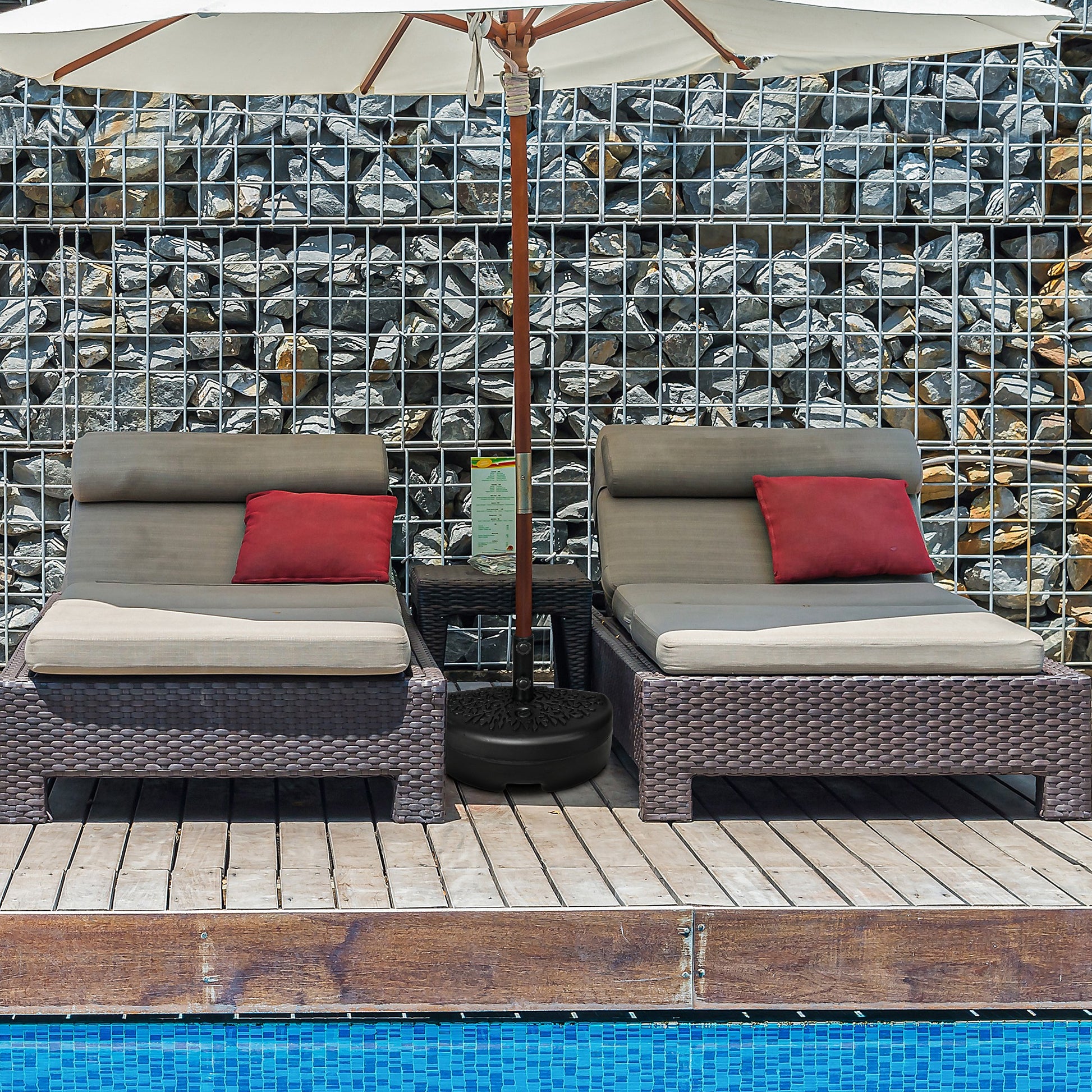 Two grey wicker patio chairs with red cushions sit on wooden deck next to pool