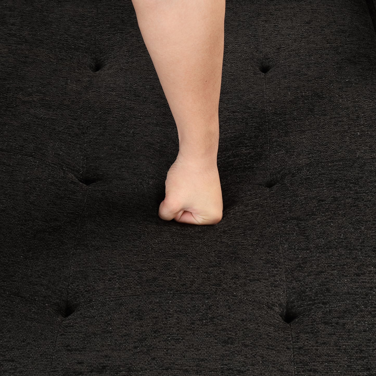 Dark charcoal textured fabric sofa with button tufting and a persons fist pressing into cushion