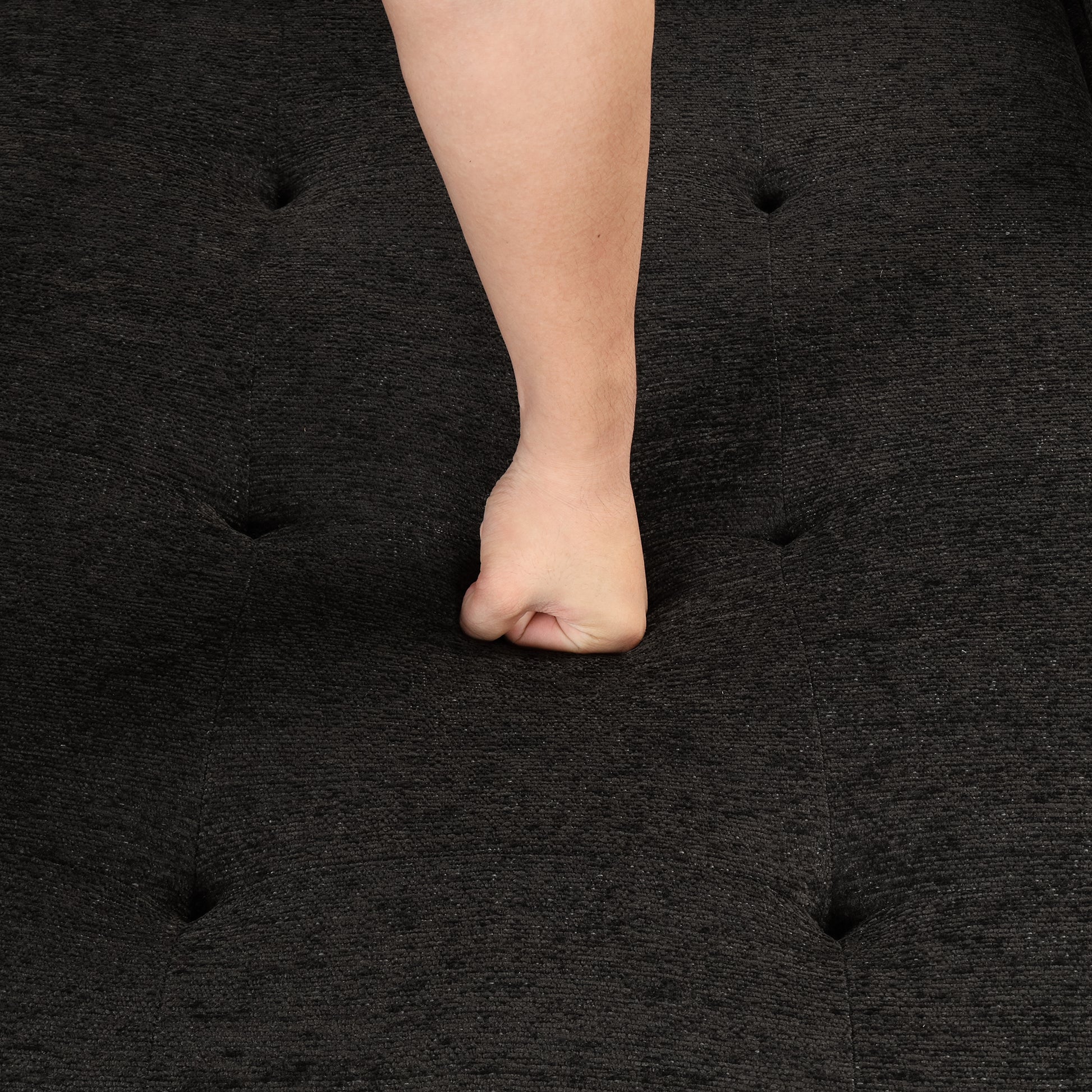 Dark charcoal textured fabric sofa with button tufting and a persons fist pressing into cushion