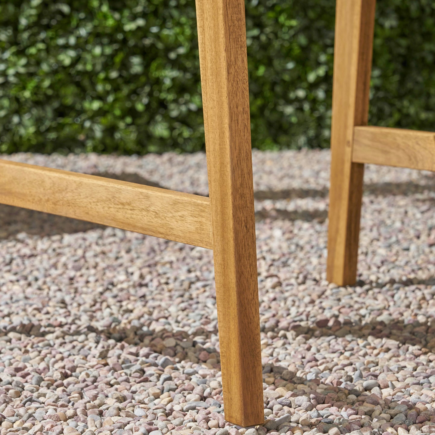 Closeup of wooden bar stool legs with a gravel and greenery background