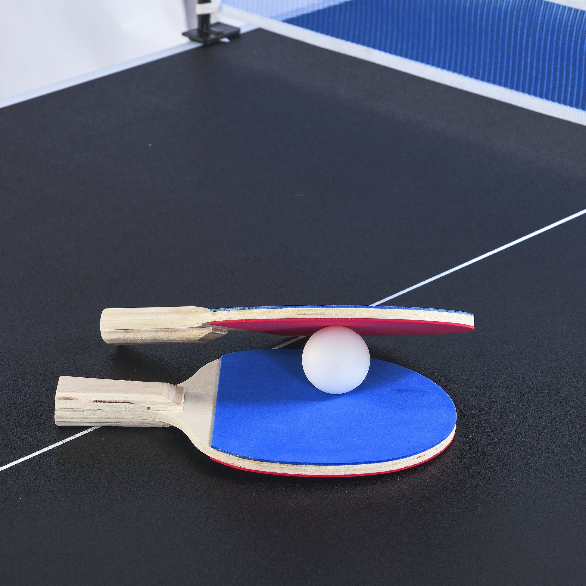 Blue and red ping pong paddle with white ball on black table