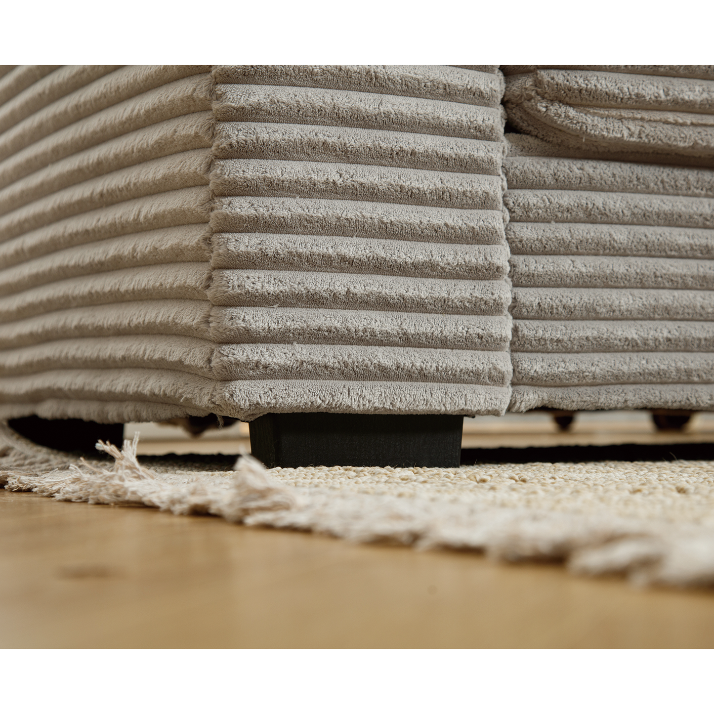 Closeup of beige corduroy sofa fabric with textured stripes and a dark wood leg