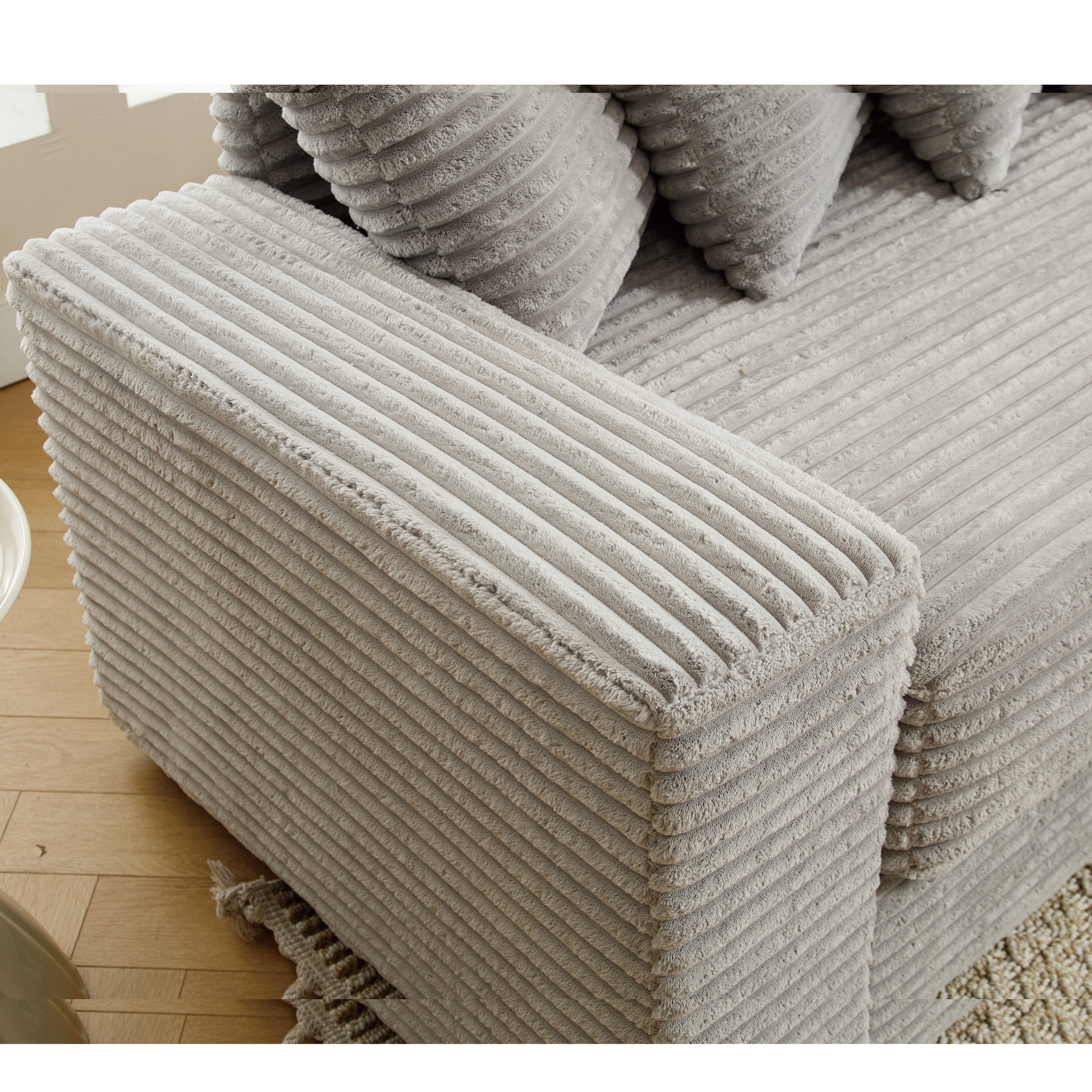 Closeup of a plush grey corduroy sectional sofa armrest with ribbed texture