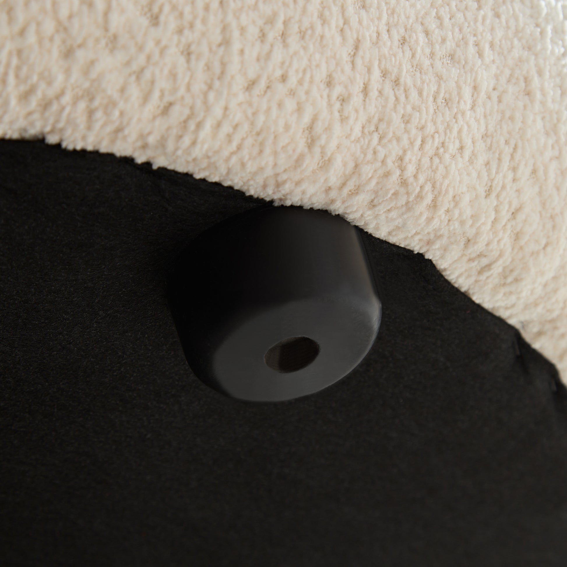 Closeup of a black plastic furniture foot attached to a cream sherpa fabric