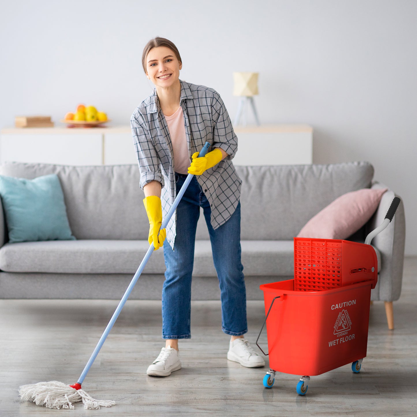 Woman in yellow gloves mopping floor with a white string mop and red bucket