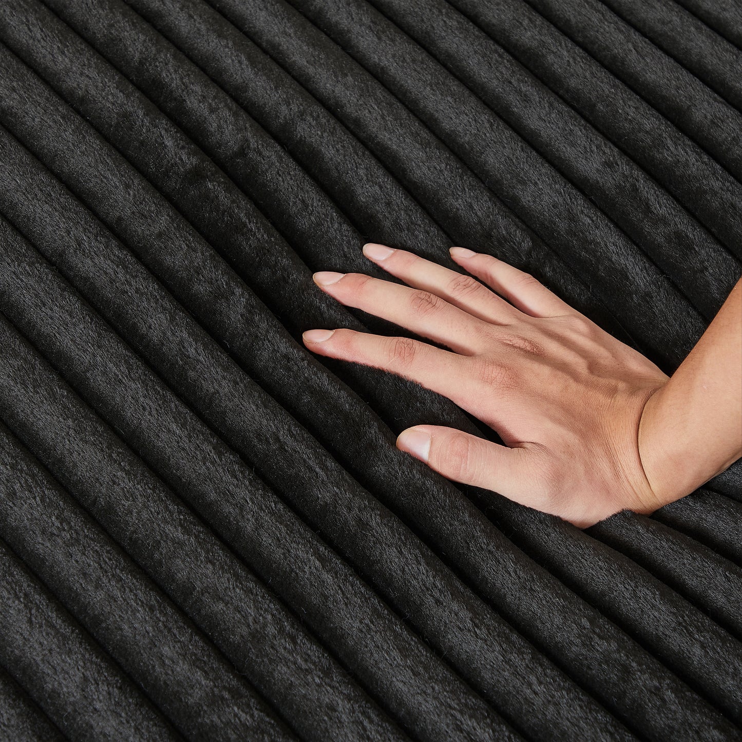 Closeup of a hand touching a plush black corduroy fabric with deep soft ridges